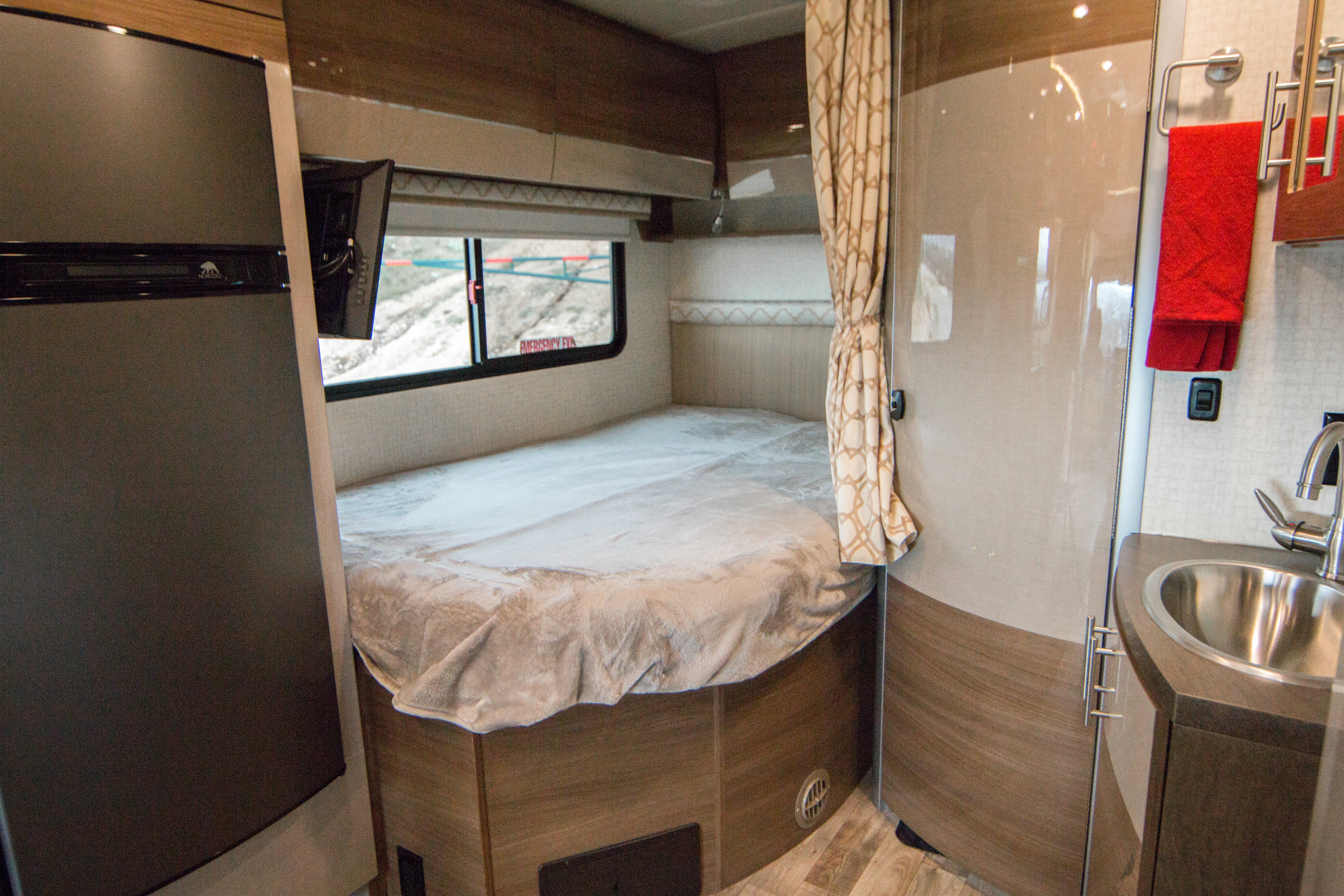 Cozy RV rental interior featuring a comfortable bed, compact kitchenette, and refrigerator for on-the-road living.. Itasca Navion 2017