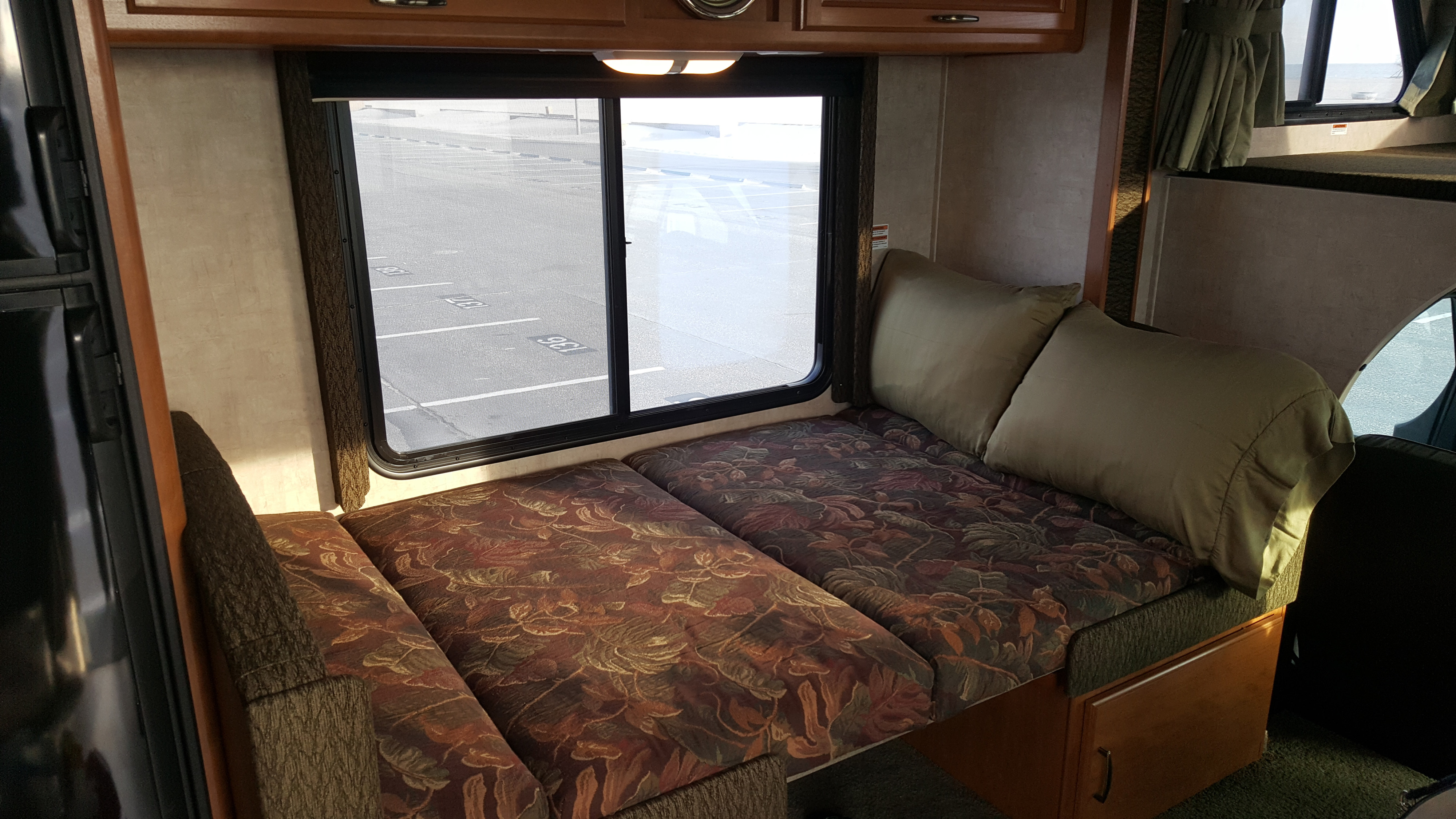 Inside an RV rental: a cozy dinette with patterned cushions and pillows, overlooking a parking lot. Converts to a bed.. Fleetwood Tioga 2005