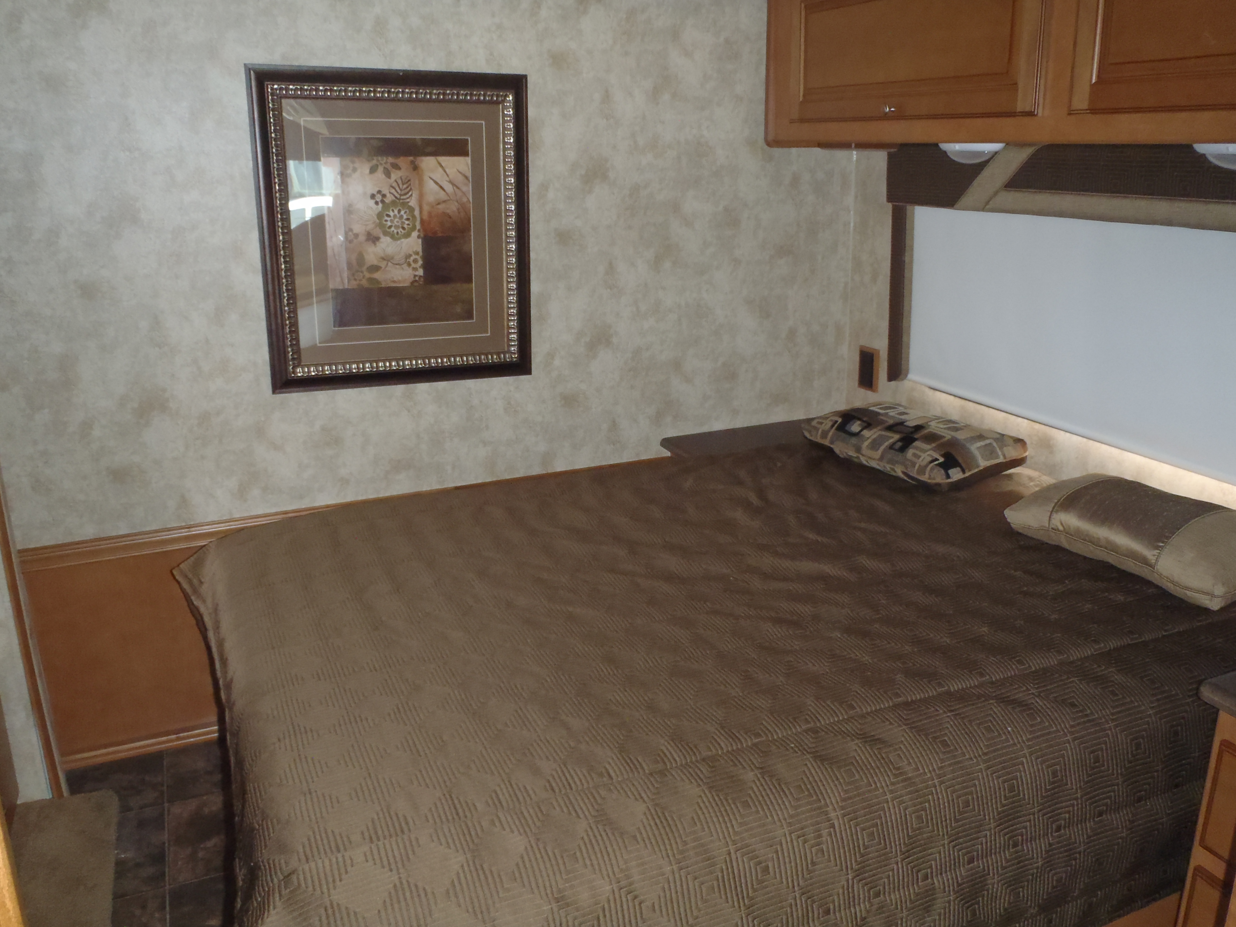 RV rental interior: cozy bedroom with quilted bedspread, overhead cabinets, and framed artwork.. Winnebago Sunstar 2012