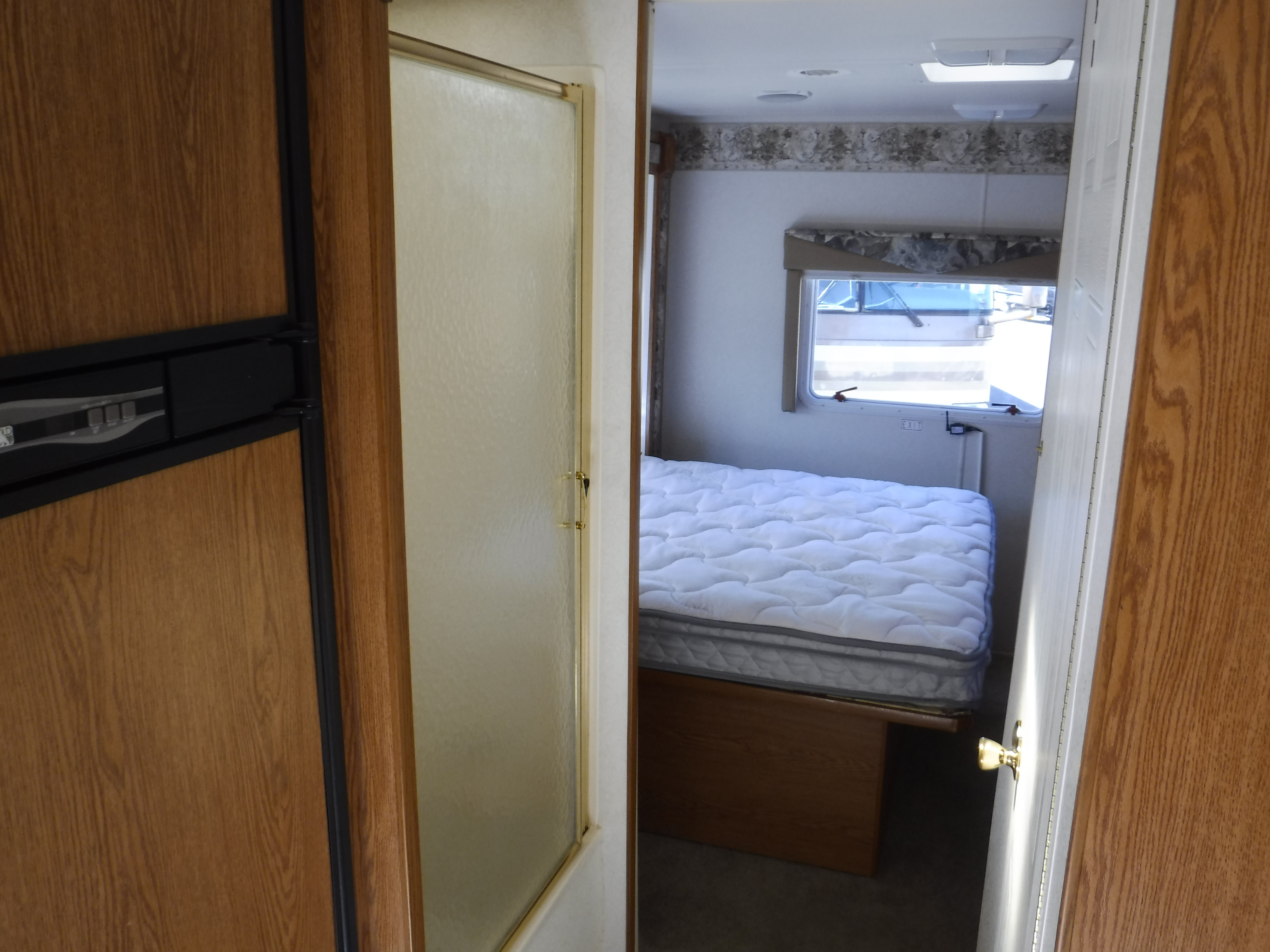 Inside an RV rental: view of the compact bedroom with a window, a frosted shower, and a built-in refrigerator.. HOLIDAY RAMBLER ATLANTIS 2002