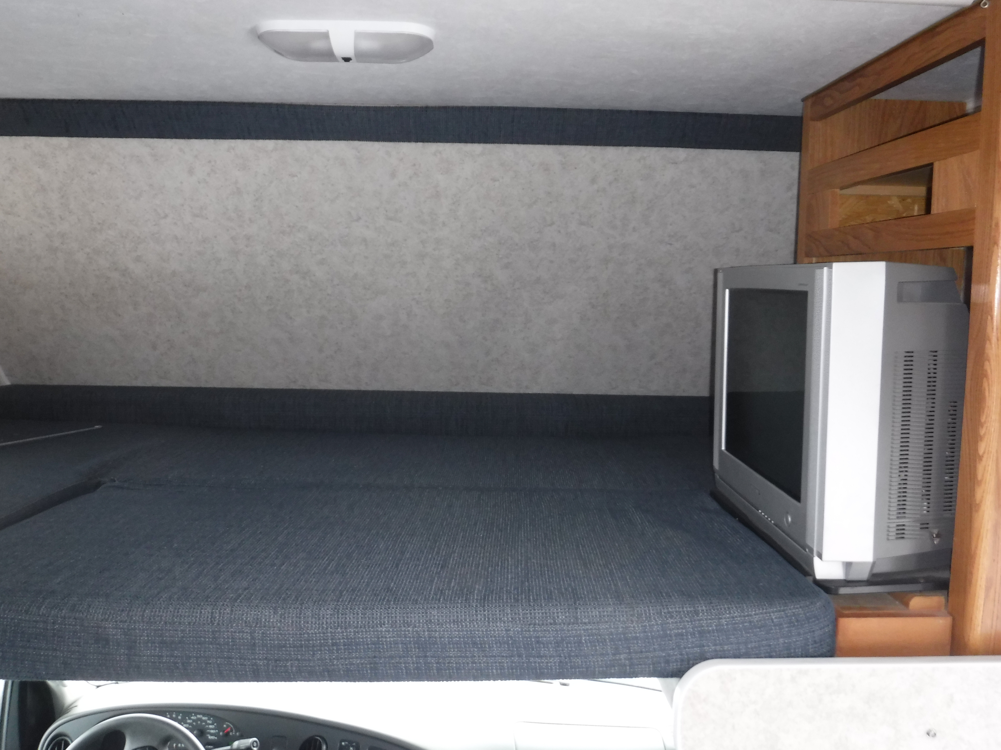 Inside an RV rental, showing a dark blue bunk bed with a vintage CRT TV at its end. The vehicle dashboard is visible below.. GULF STREAM YELLOWSTONE 2005
