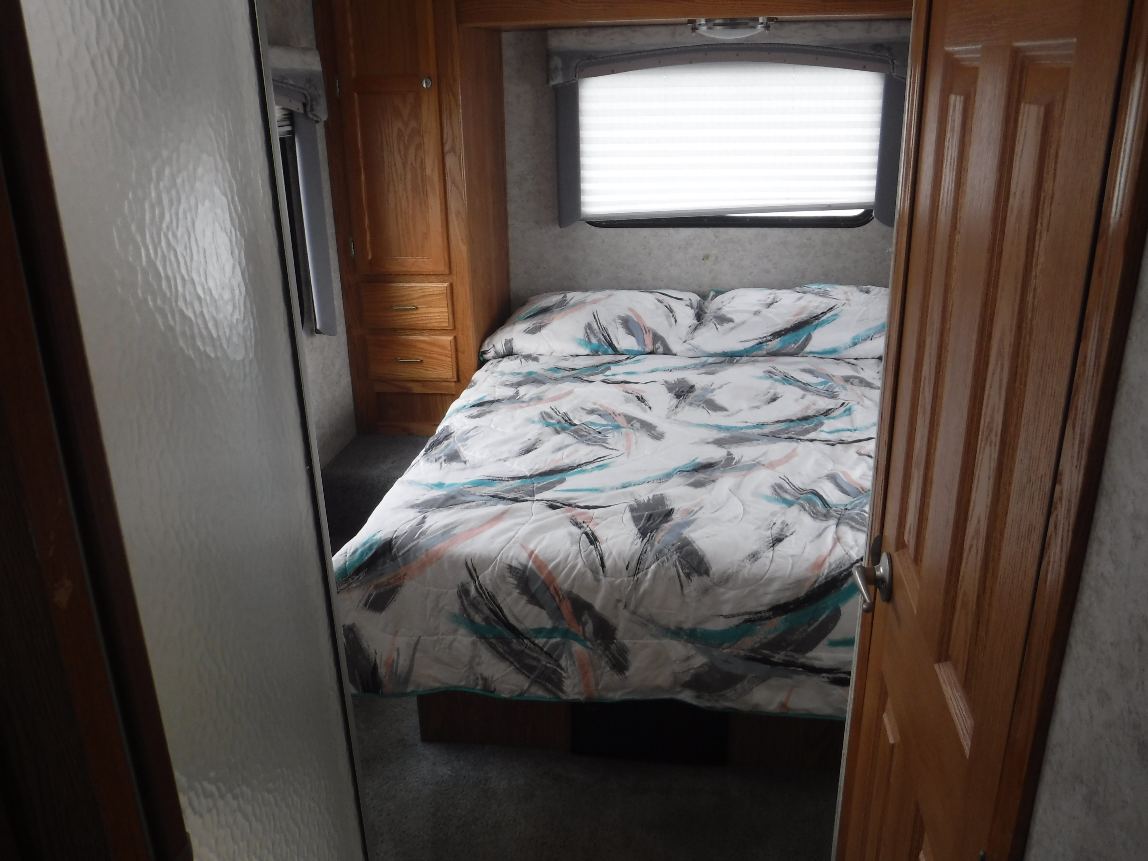 Cozy RV rental bedroom with a comfortable bed, patterned comforter, window with blinds, and wood storage cabinet.. GULF STREAM YELLOWSTONE 2005
