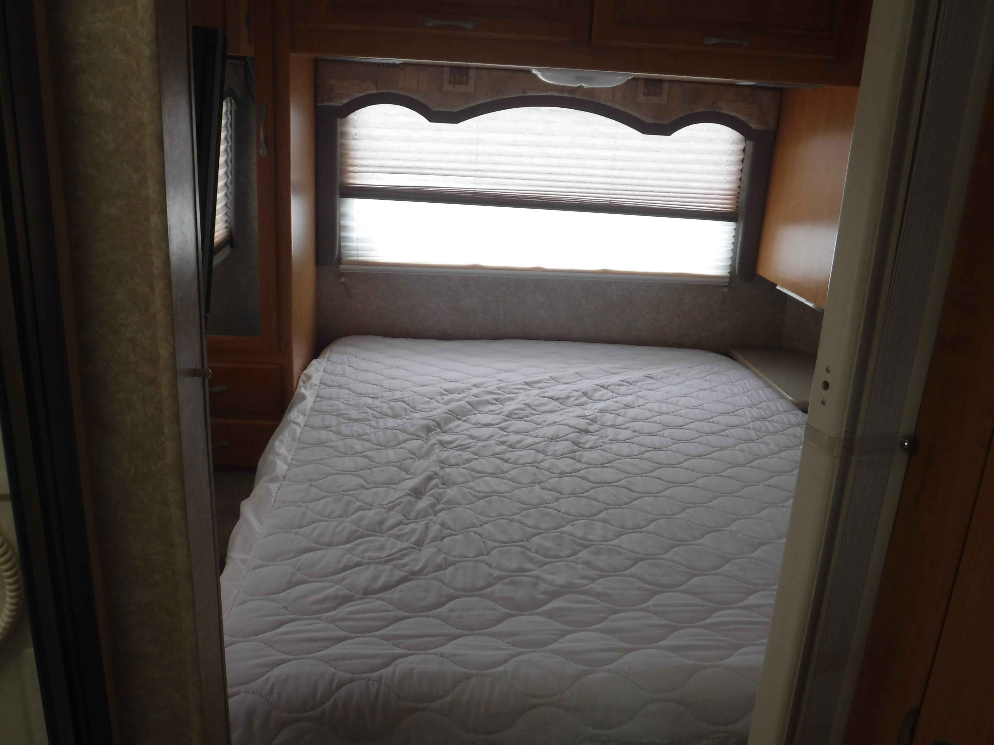 Inside an RV rental: a neat bedroom with a large white quilted bed, window with blinds, and wood storage cabinets.. CHATEAU SPORT 2007
