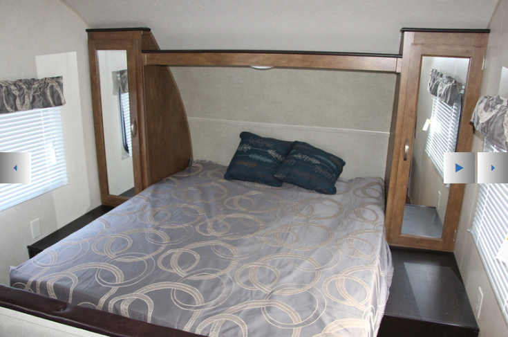 Cozy RV rental bedroom features a bed with pillows, two windows, and mirrored wardrobes for compact storage.. Forest River Wildwood X-Lite 2018