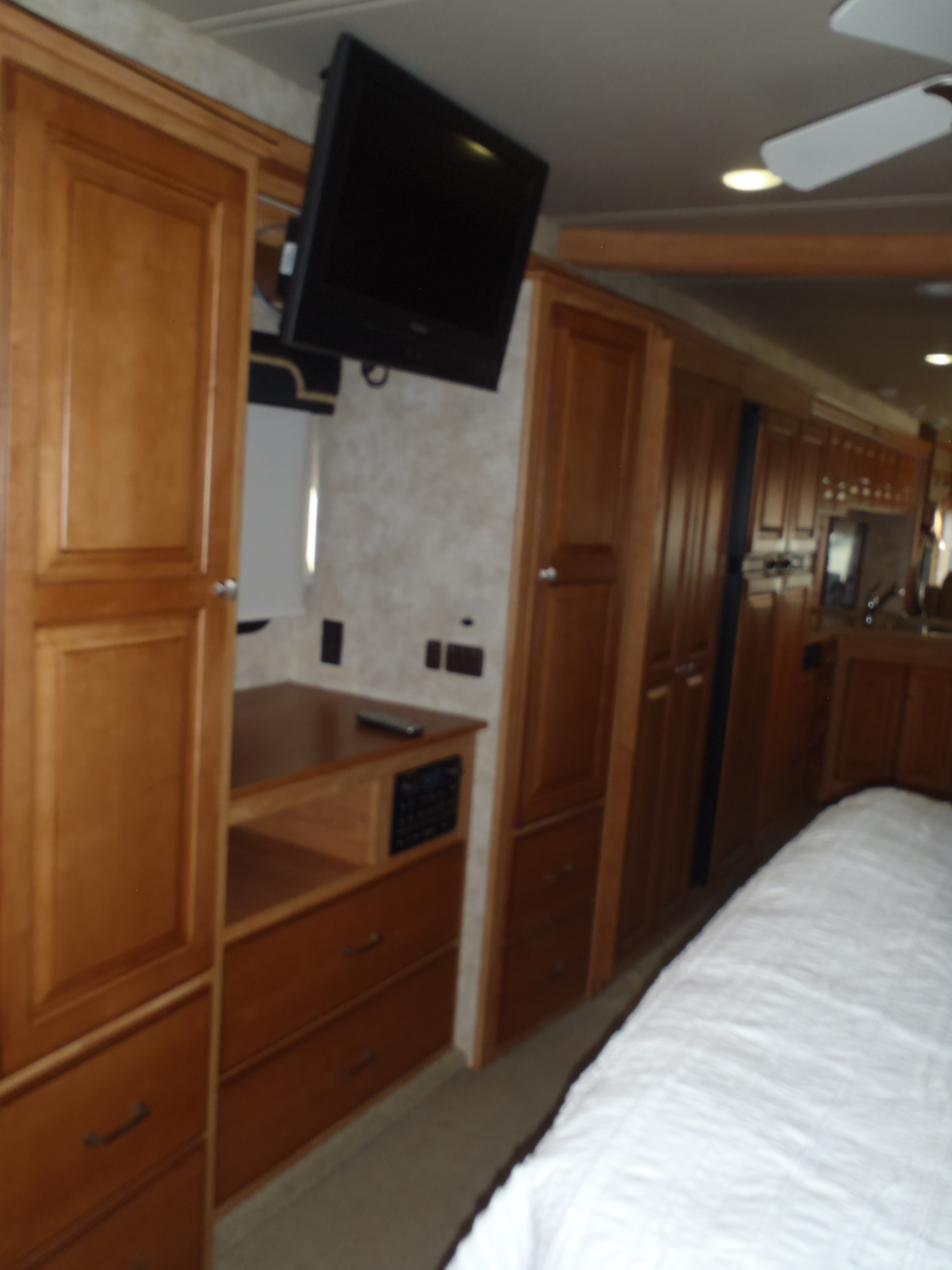 RV rental bedroom: wooden cabinets, drawers, wall-mounted TV, white bed, and ceiling fan provide comfort.. Itasca Suncruiser 2017