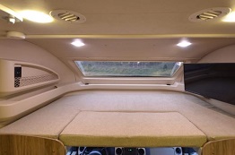 Cozy overcab sleeping area in this modern RV rental, featuring a bright skylight, comfortable bed, and TV.. Jayco Envoy 31L 2018