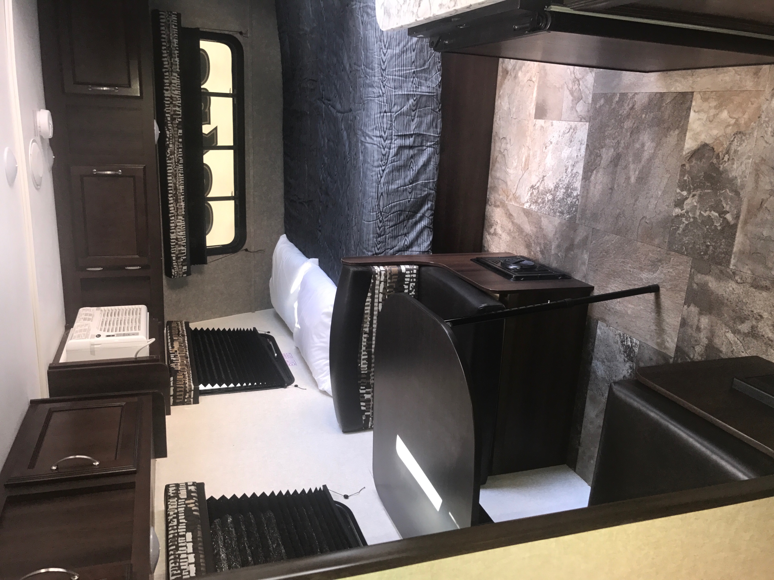 Compact RV rental interior featuring a functional bedroom, kitchen, and dining area with dark wood and patterned flooring.. Jayco Jay Flight 2018