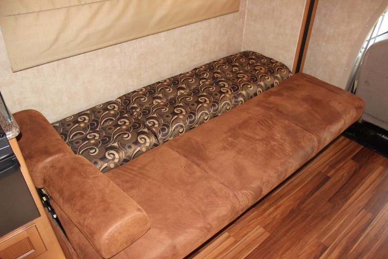 RV rental interior: convertible sofa bed with patterned backrest & wood floor, ideal for compact living.. Forest River Coachmen Freelander 2013