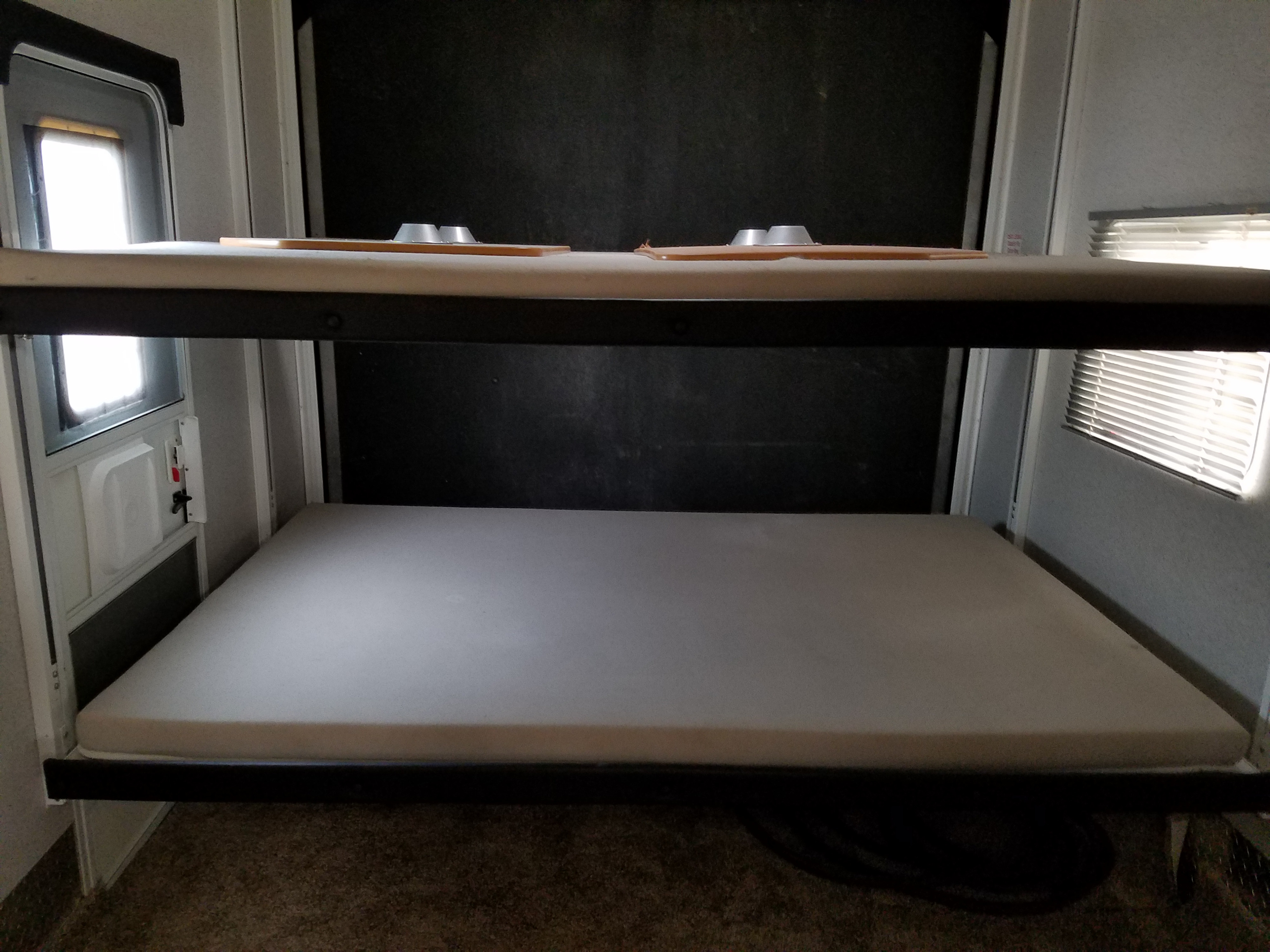 An RV rental's sleeping area with sturdy upper and lower bunk beds, complete with mattresses. A door and window are seen.. Heartland Cyclone 2009