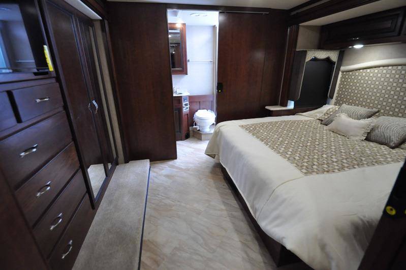 Spacious RV rental bedroom featuring a comfortable bed, dark wood dresser with TV, and an en-suite bathroom.. Holiday Rambler Vacationer 2017