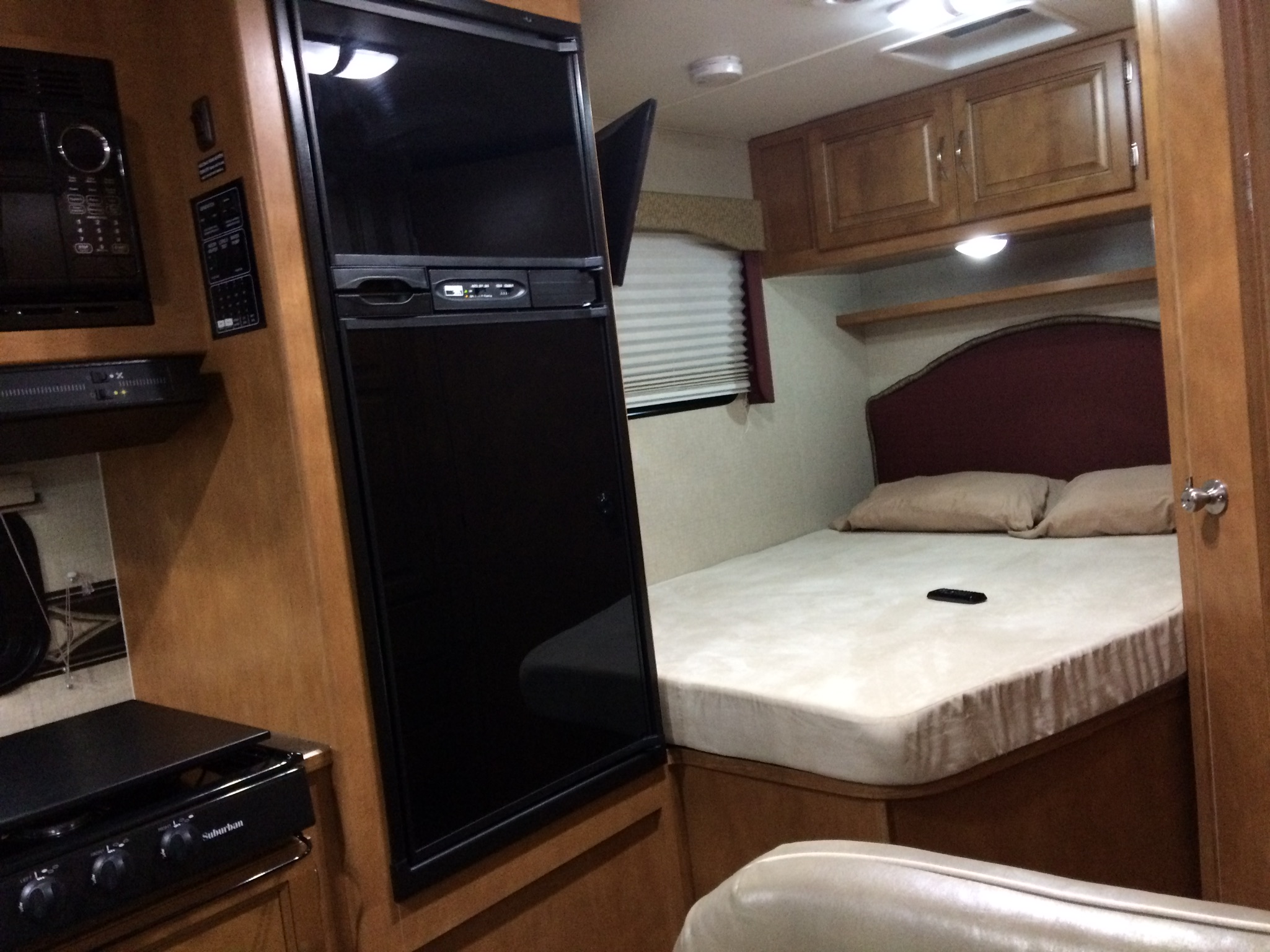 RV rental interior featuring a kitchen with microwave, fridge, and a bedroom with a bed, cabinets, and window.. Itasca Spirit 2014