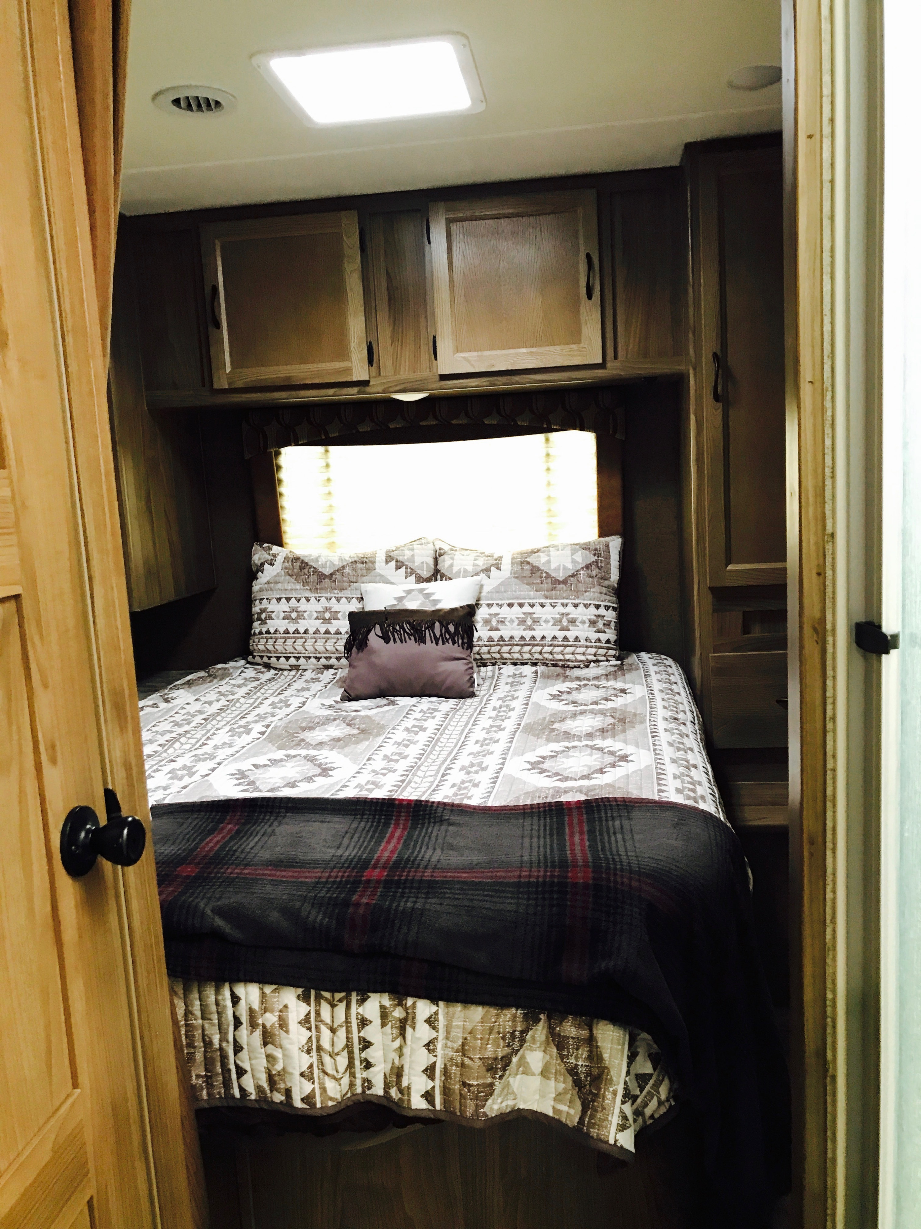 Cozy RV rental bedroom with patterned bedding, plaid blanket, and wood cabinets.. Coachmen Freelander 2017