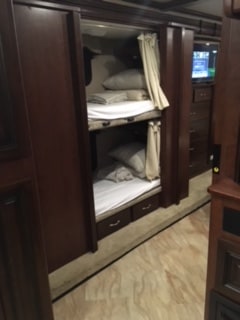 Cozy dark wood RV rental interior showing two bunk beds with curtains and bedding. Ideal for family travel.. Holiday Rambler Vacationer 2017