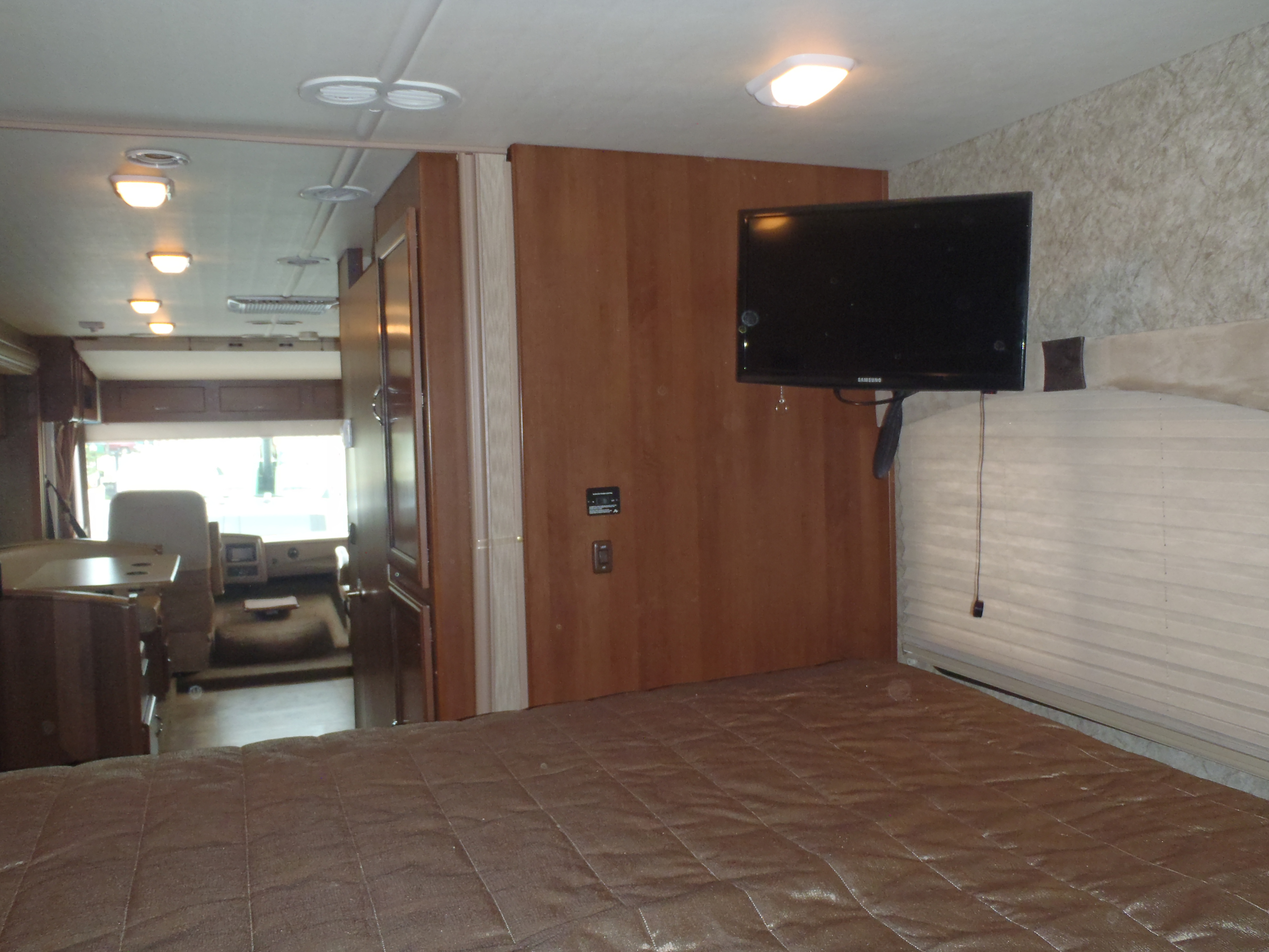 Inside an RV rental: Cozy bedroom area with a bed, wall TV, and a glimpse of the front cabin.. Fleetwood Storm 2015