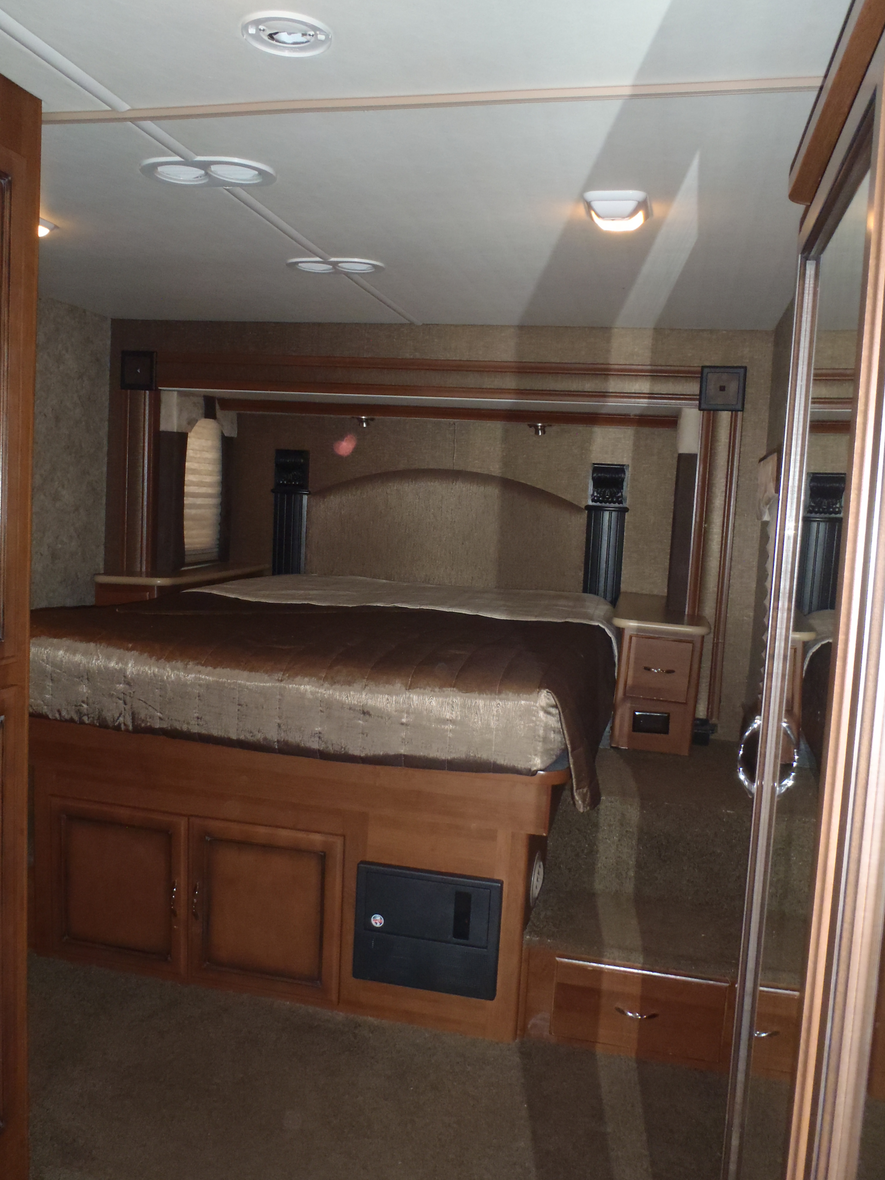 Comfortable RV rental master bedroom featuring a large bed, built-in storage, and ambient overhead lighting.. Fleetwood Storm 2015