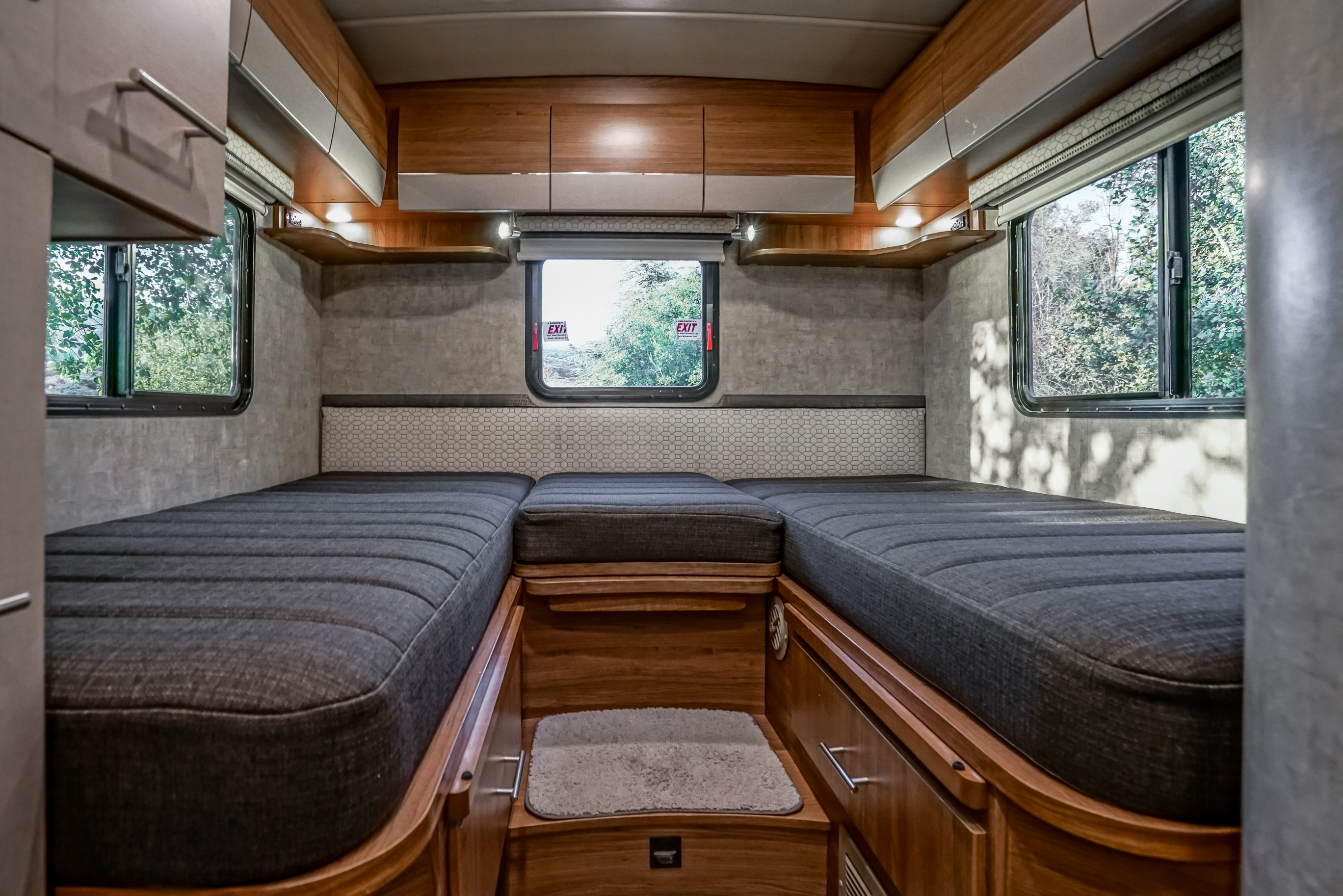 Inside a cozy **rv rental**: two beds, wooden storage, and windows framing outdoor greenery create a compact sleeping area.. Winnebago View 2018