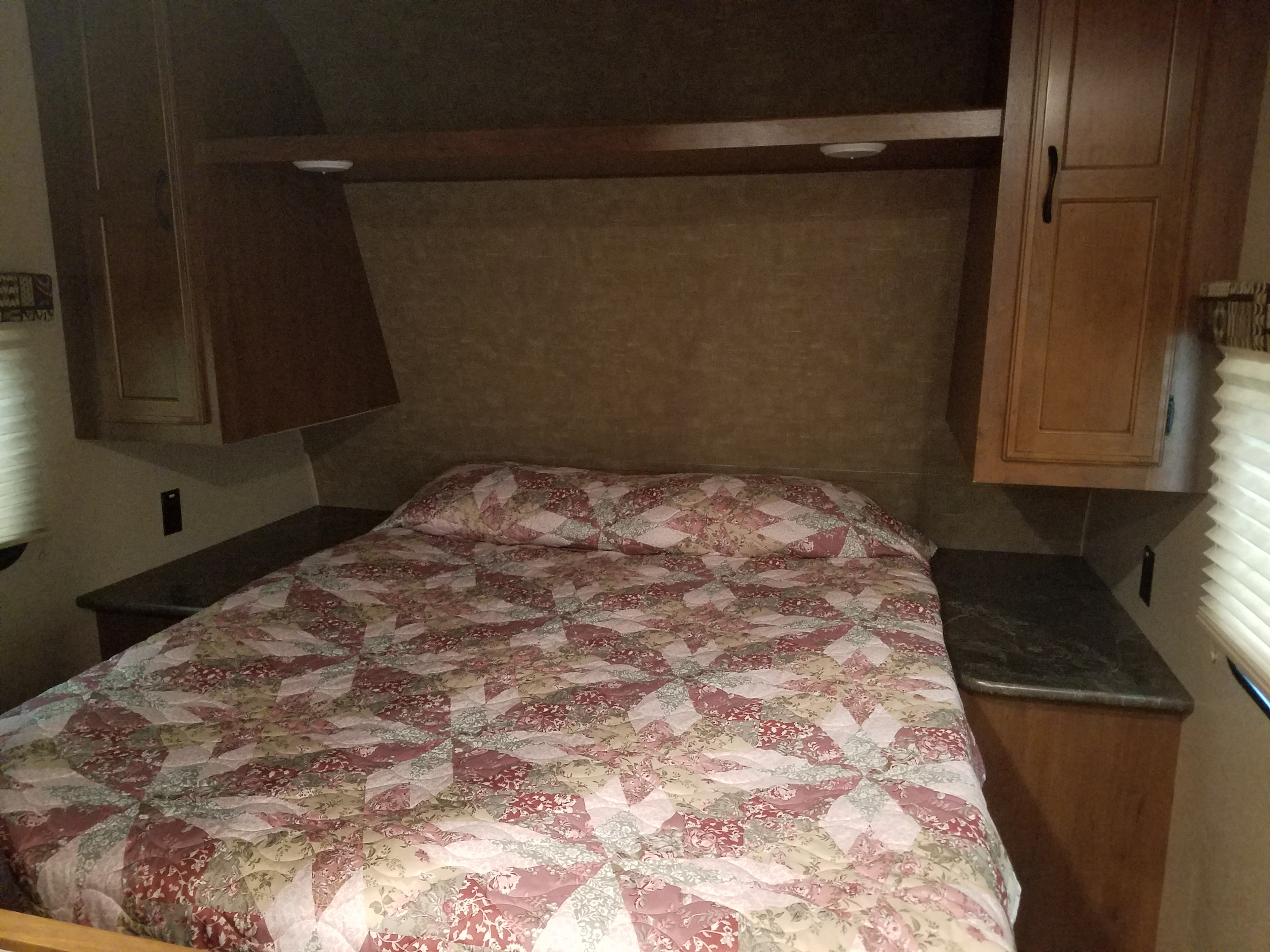Compact RV rental bedroom with a patterned quilt, overhead cabinets, and side shelves.. Jayco Jay Flight 2016