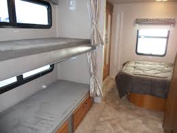 Inside an RV rental, a cozy sleeping area with bunk beds (bottom with storage) and a main bed, ideal for family adventures.. Jayco Redhawk 2016