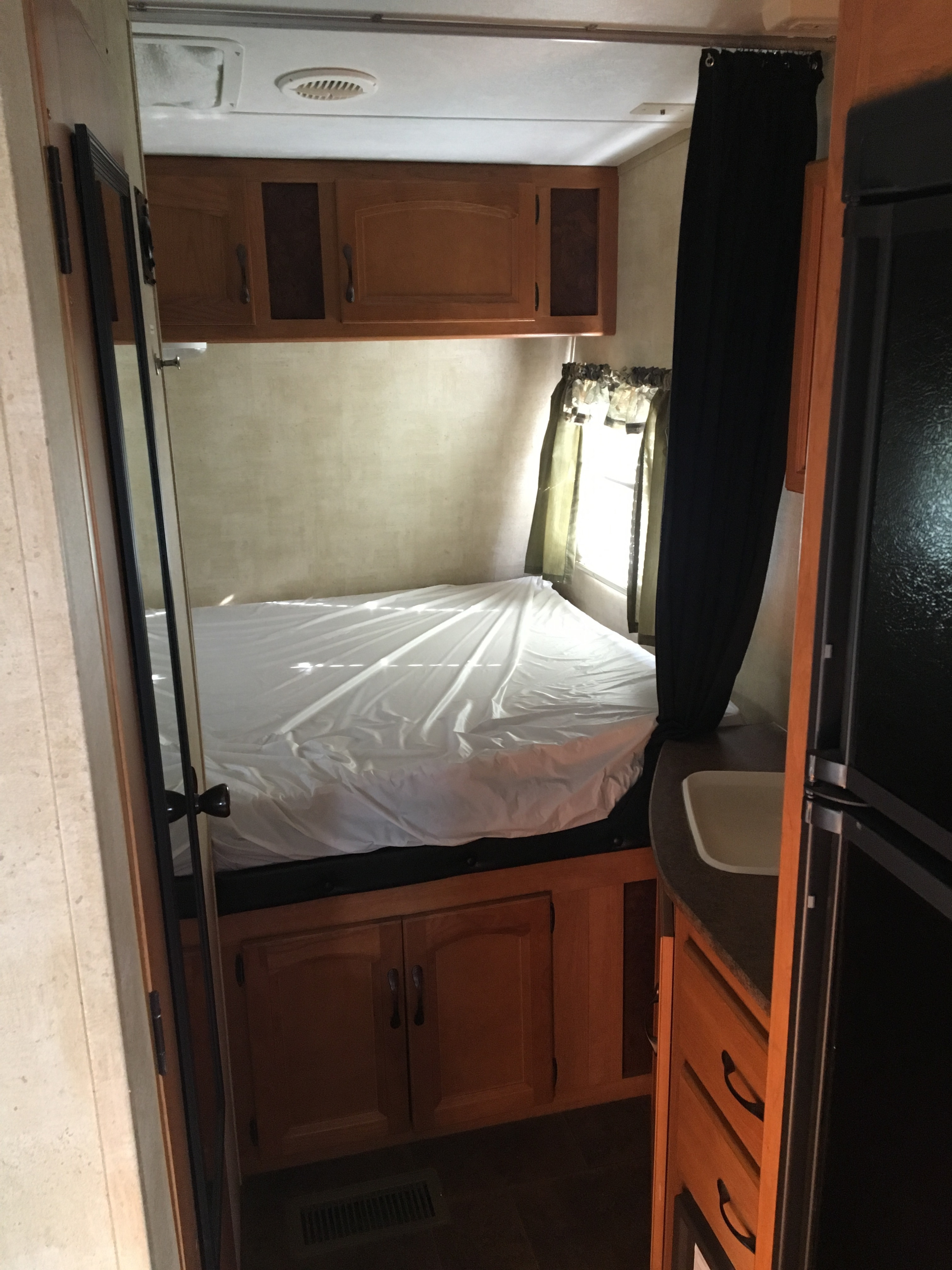 RV rental interior showcasing a compact bedroom with bed, overhead cabinets, and a small kitchen area with sink.. Keystone Energy Camper 2012
