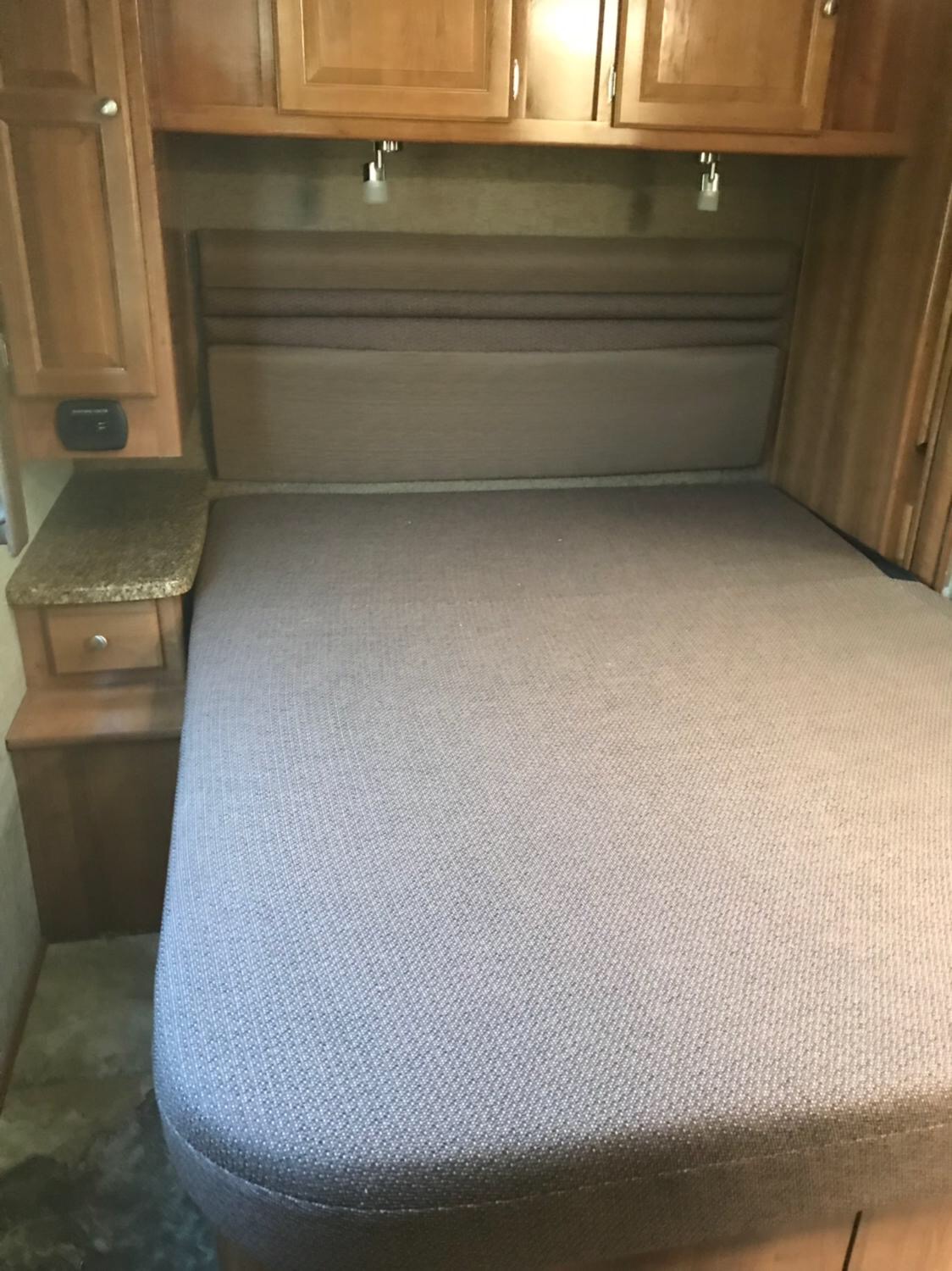 RV rental bedroom featuring a comfortable bed, overhead cabinets, nightstand, and reading lights, ready for travel.. Coachmen Leprechaun 2018