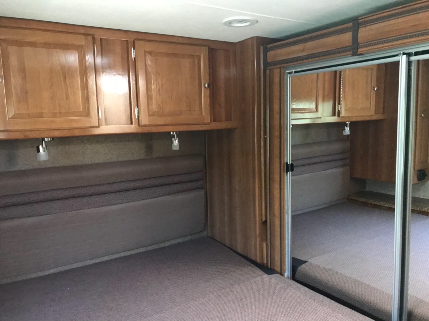 Cozy RV rental bedroom with wooden cabinets, reading lights, and a mirrored closet reflecting the compact sleeping area.. Coachmen Leprechaun 2018