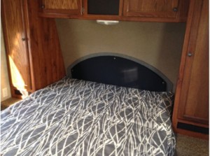 Cozy RV rental bedroom with a compact bed, headboard, and overhead/side storage cabinets, perfect for travel.. Hideout 22RB WE 2014