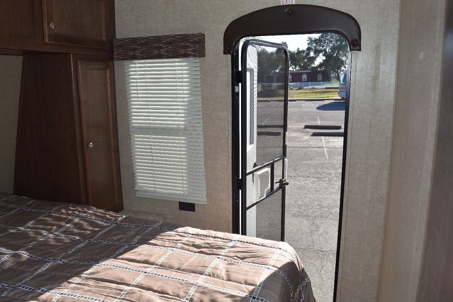 RV rental interior featuring a cozy bedroom with a patterned bedspread, storage, window, and an open screen door to the parking lot.. Keystone Hideout 2017
