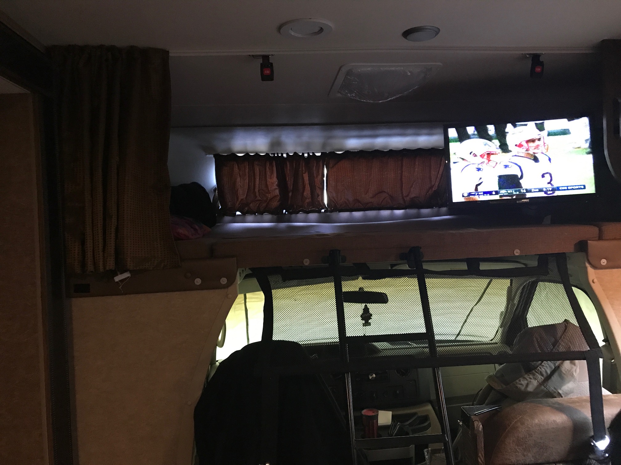 RV rental's cozy interior: overhead bunk, TV with football, and front driving cab.. Coachmen Leprechaun 2016