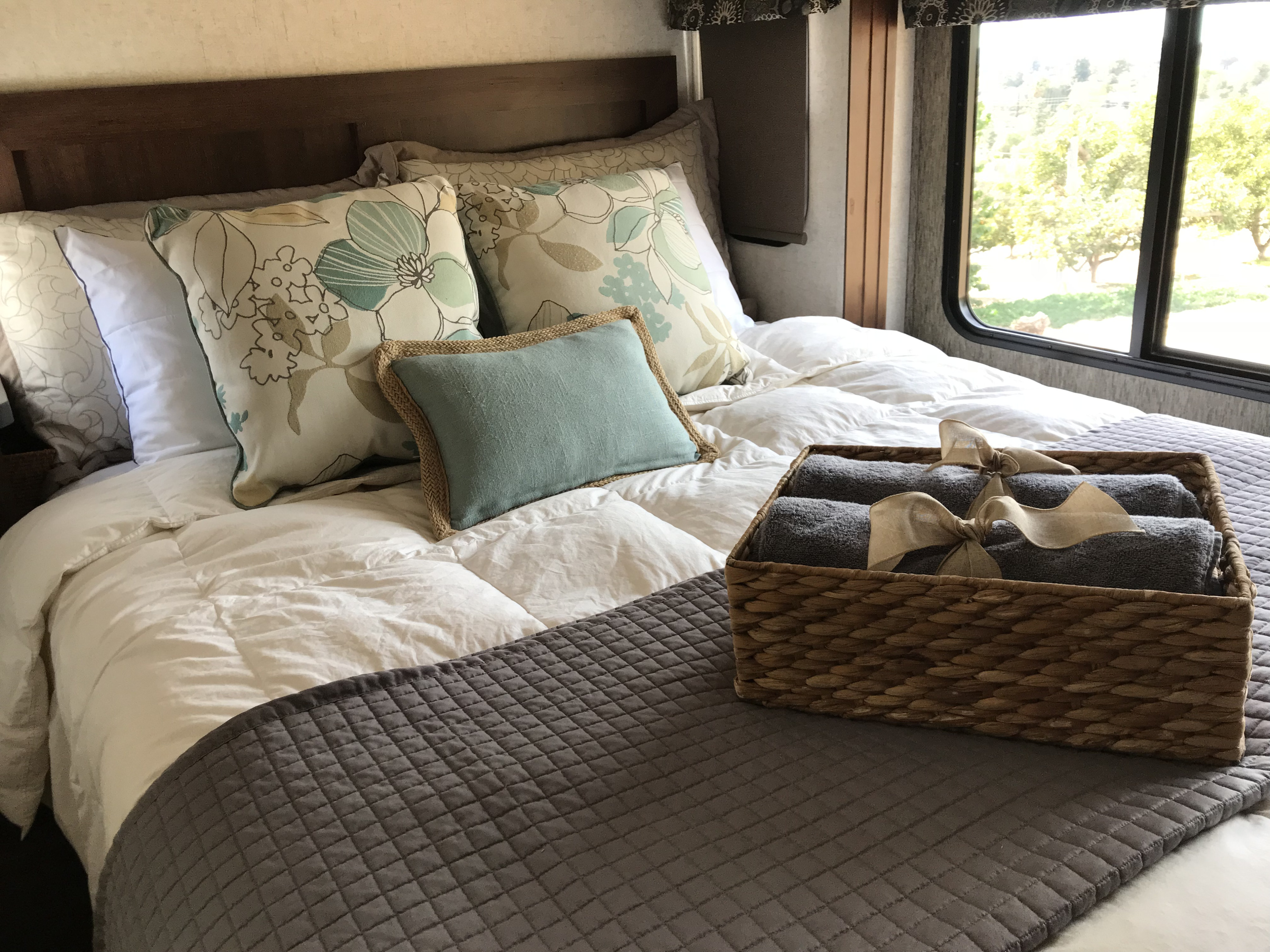 Cozy RV rental bedroom featuring a comfortable bed with patterned pillows, soft bedding, and a basket of towels.. Forest River Sunseeker 2018