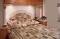 Comfortable RV rental bedroom features a patterned bed tucked under overhead storage and reading lights, perfect for travel.. Tioga Tioga Motorhome 2007