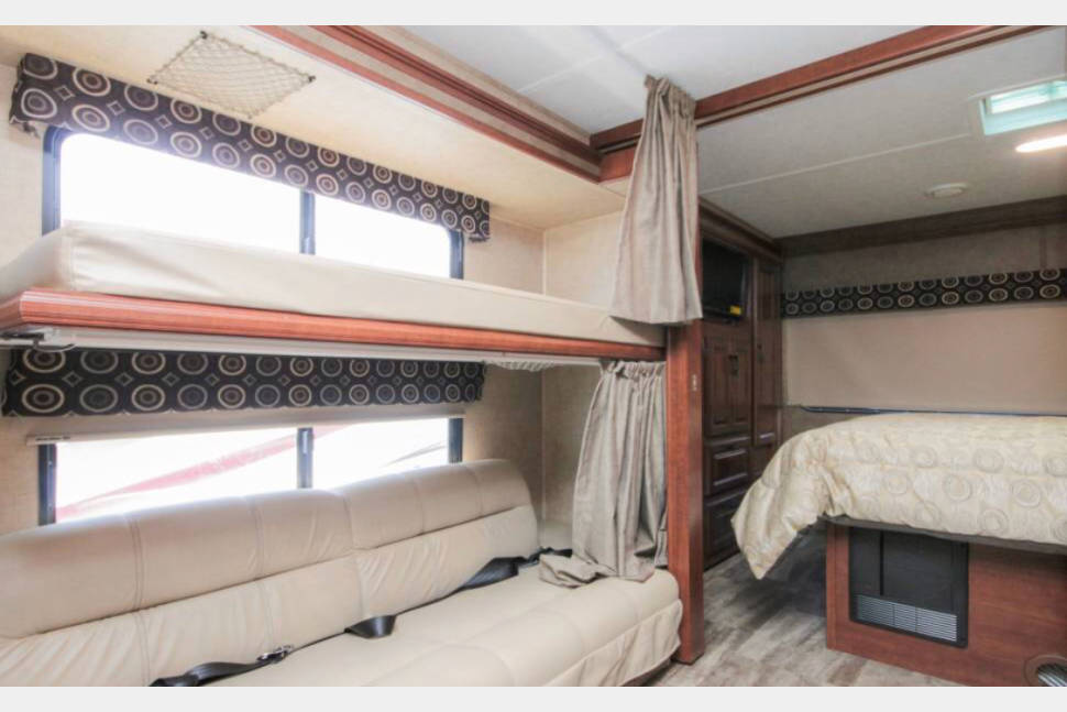 RV rental interior showcasing cozy bunk beds, a flexible sofa, and a separate main bedroom area, ideal for family travel.. Forest River Sunseeker 2017