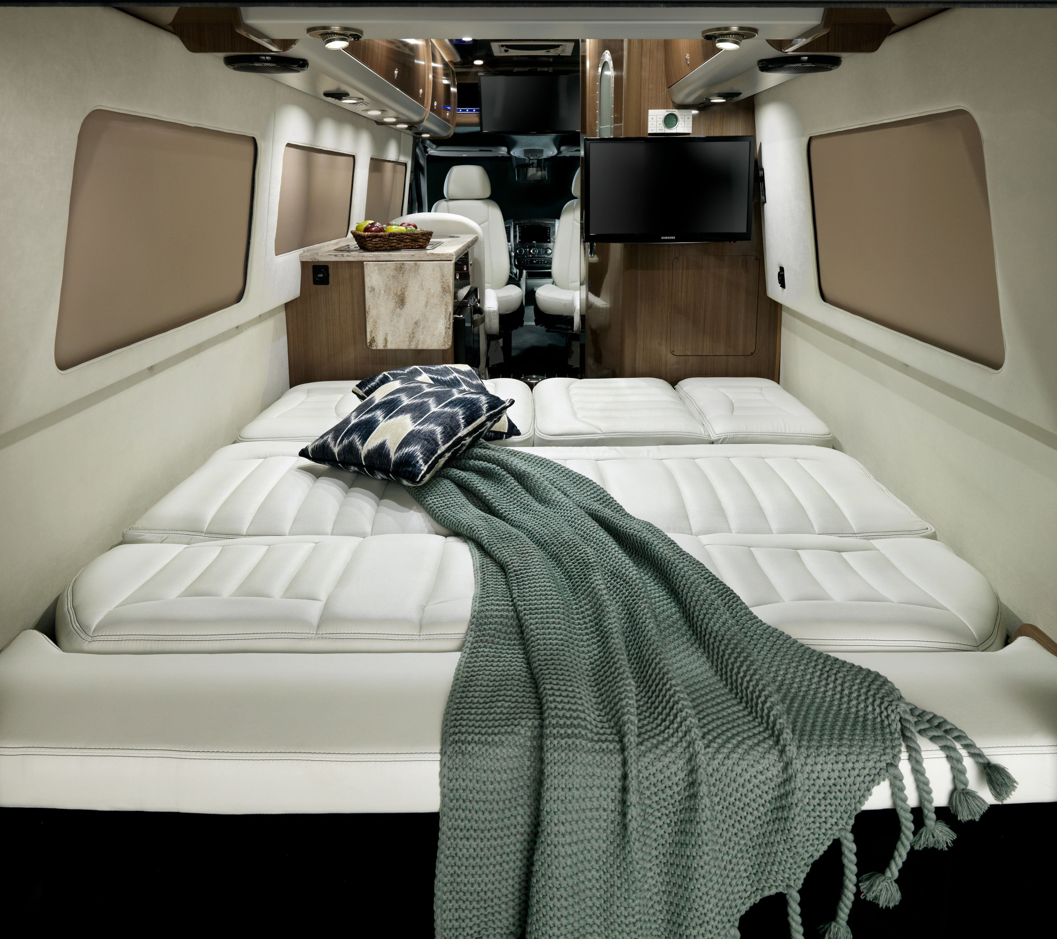 Inside a spacious RV rental: a plush white bed with throw, kitchenette, and front cabin area, offering ultimate comfort for travel.. Airstream Interstate 2014