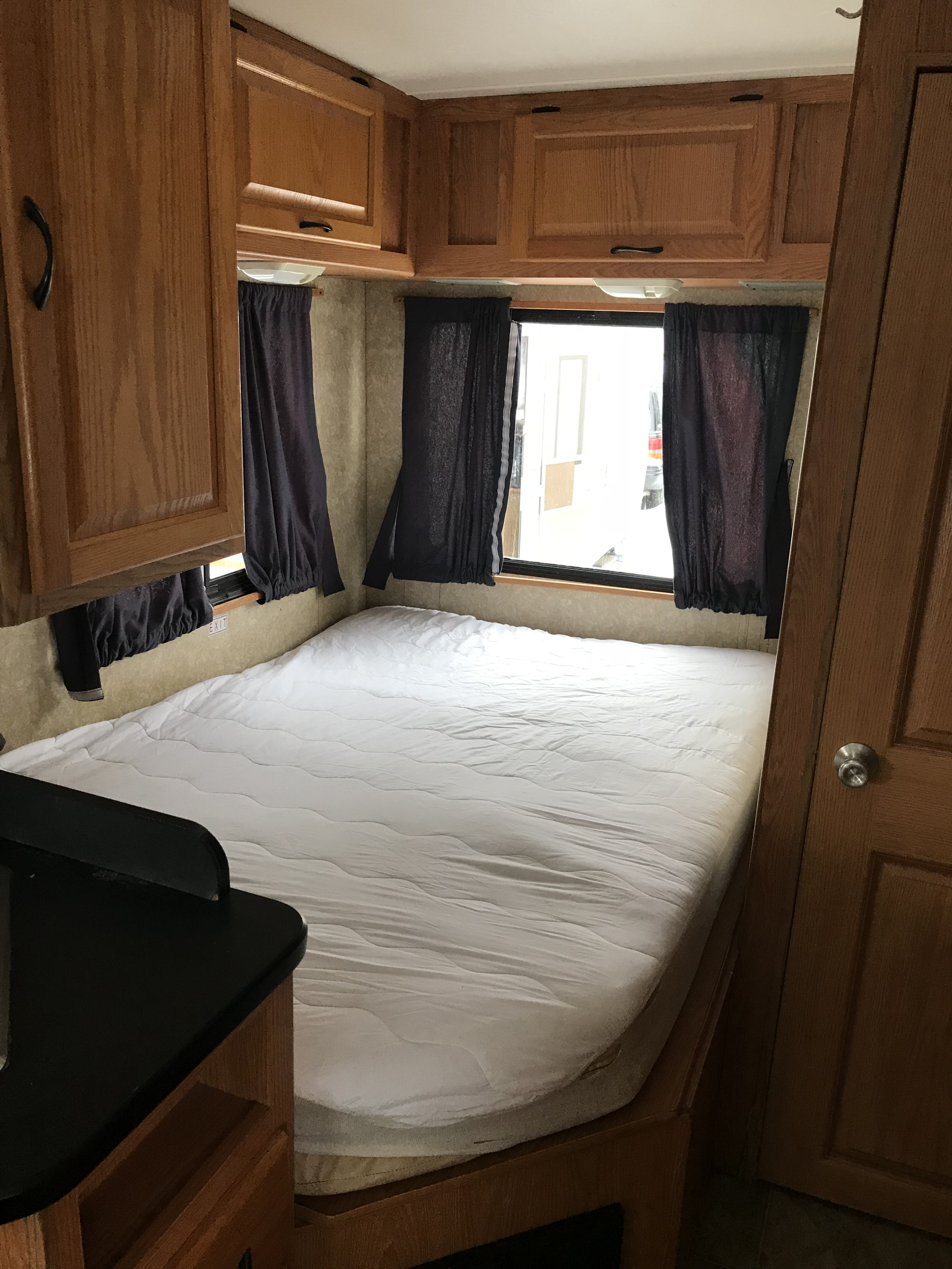 RV rental interior: A clean bed, wood cabinetry, and windows with dark curtains in a compact bedroom.. Four Winds Majestic 23A 2007