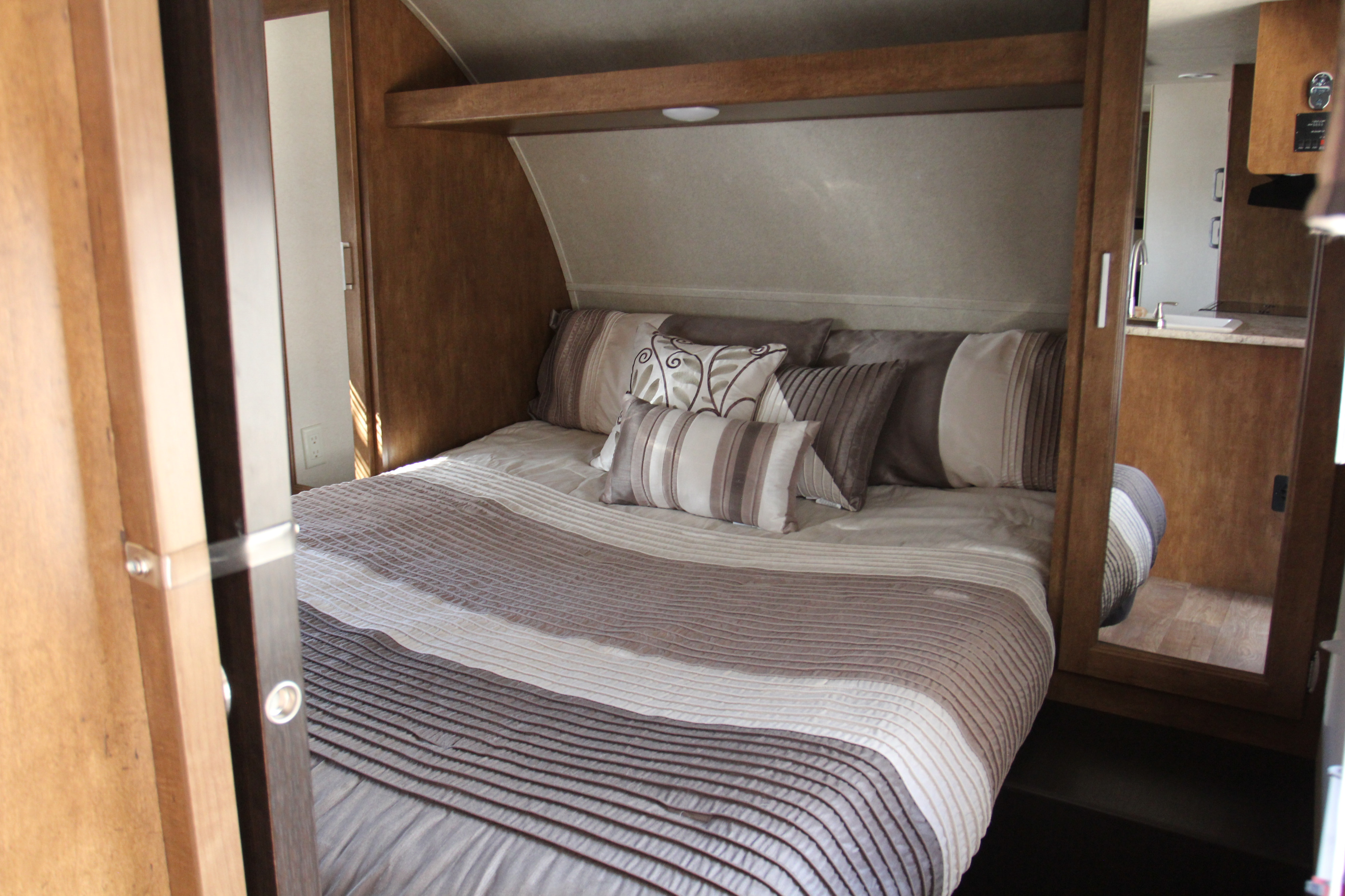 Cozy RV rental bedroom featuring a bed with neutral bedding, wood cabinetry, and a mirror reflecting the interior.. Forest River Wildwood X-Lite 2018