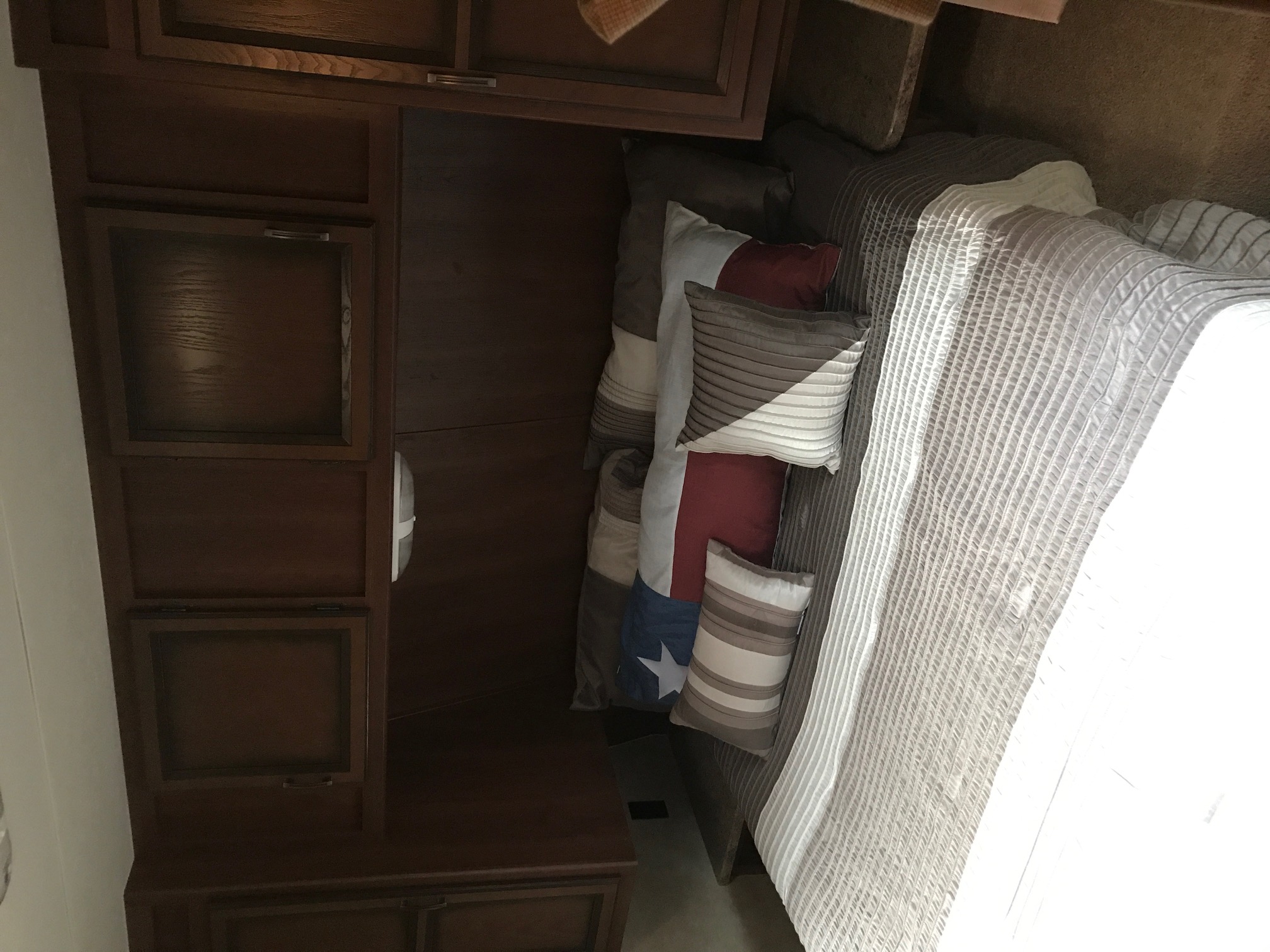 RV rental bedroom: Features a plush bed with textured comforter, decorative pillows (one Texas flag), and dark wood cabinetry.. Crossroads Longhorn 2014
