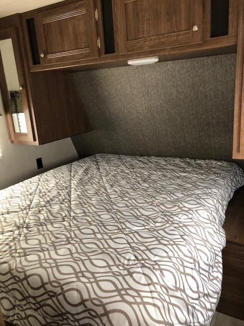 Cozy RV rental bedroom featuring a patterned bed comforter and ample overhead wooden cabinetry.. Heartland Pioneer 2018