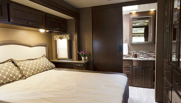 Modern RV rental interior showing a cozy bedroom with a large bed, smart storage, and an attached compact bathroom. Perfect for trips.. Thor Motor Coach 35m 2017