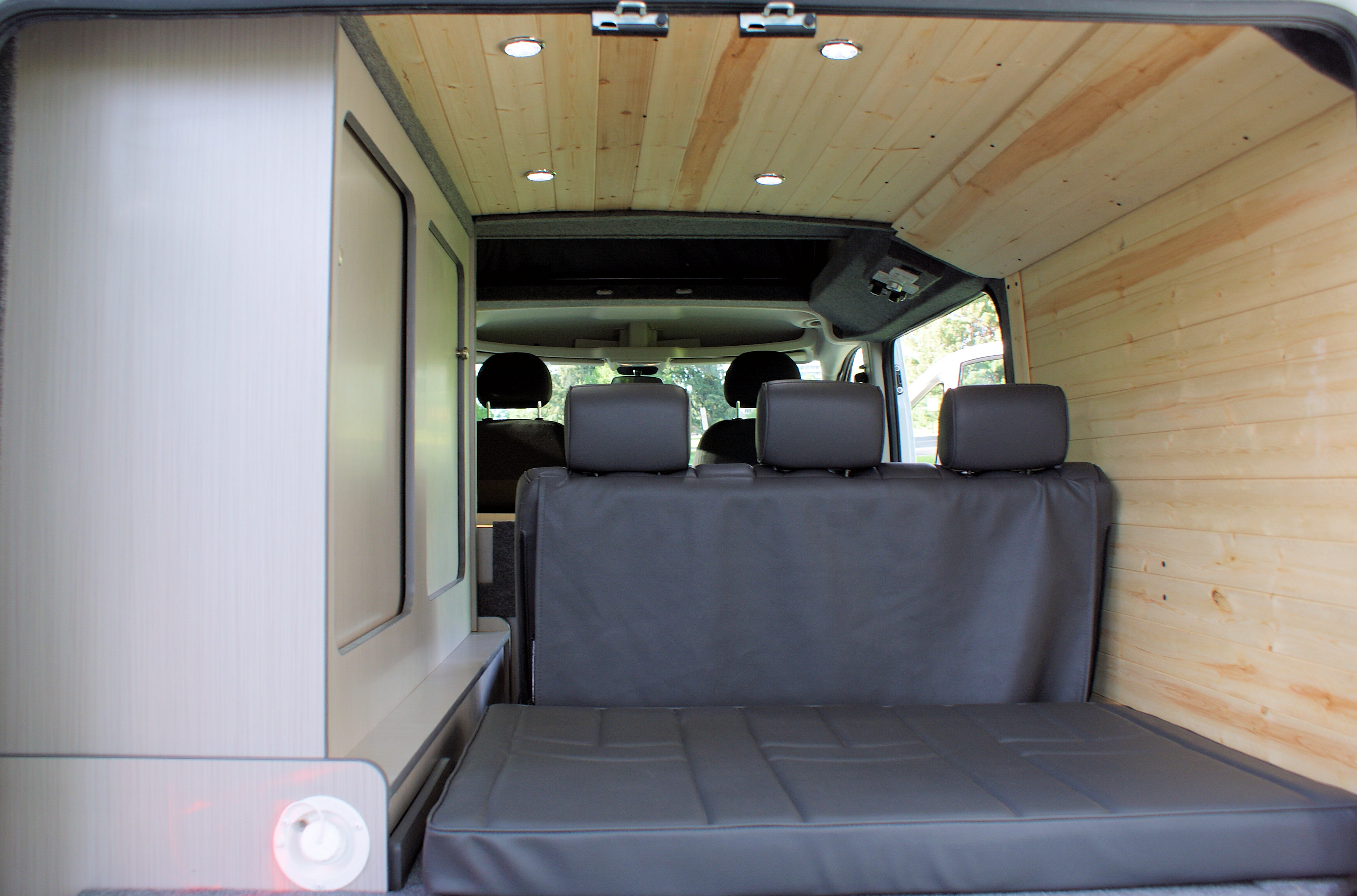 Inside an RV rental: light wood paneling, gray folding bed/seating, and light-colored interior cabinets.. Dodge Promaster 2017