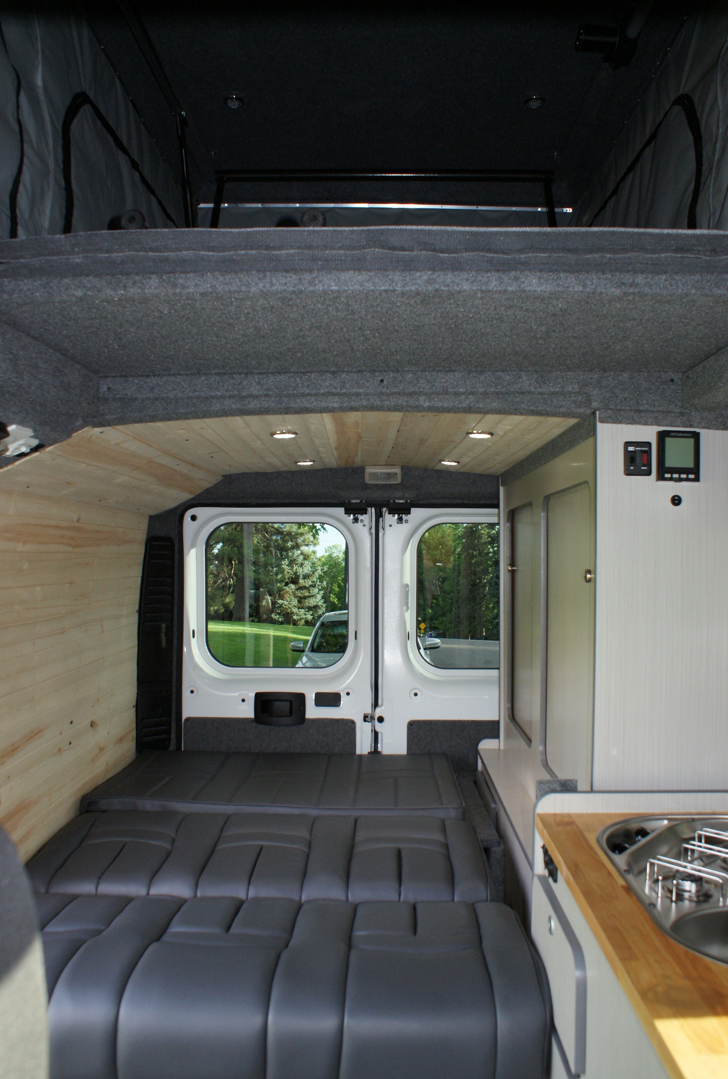 Spacious RV rental interior showing a convertible bed, overhead bunk, wood ceiling with lights, and a full kitchen.. Dodge Promaster 2017
