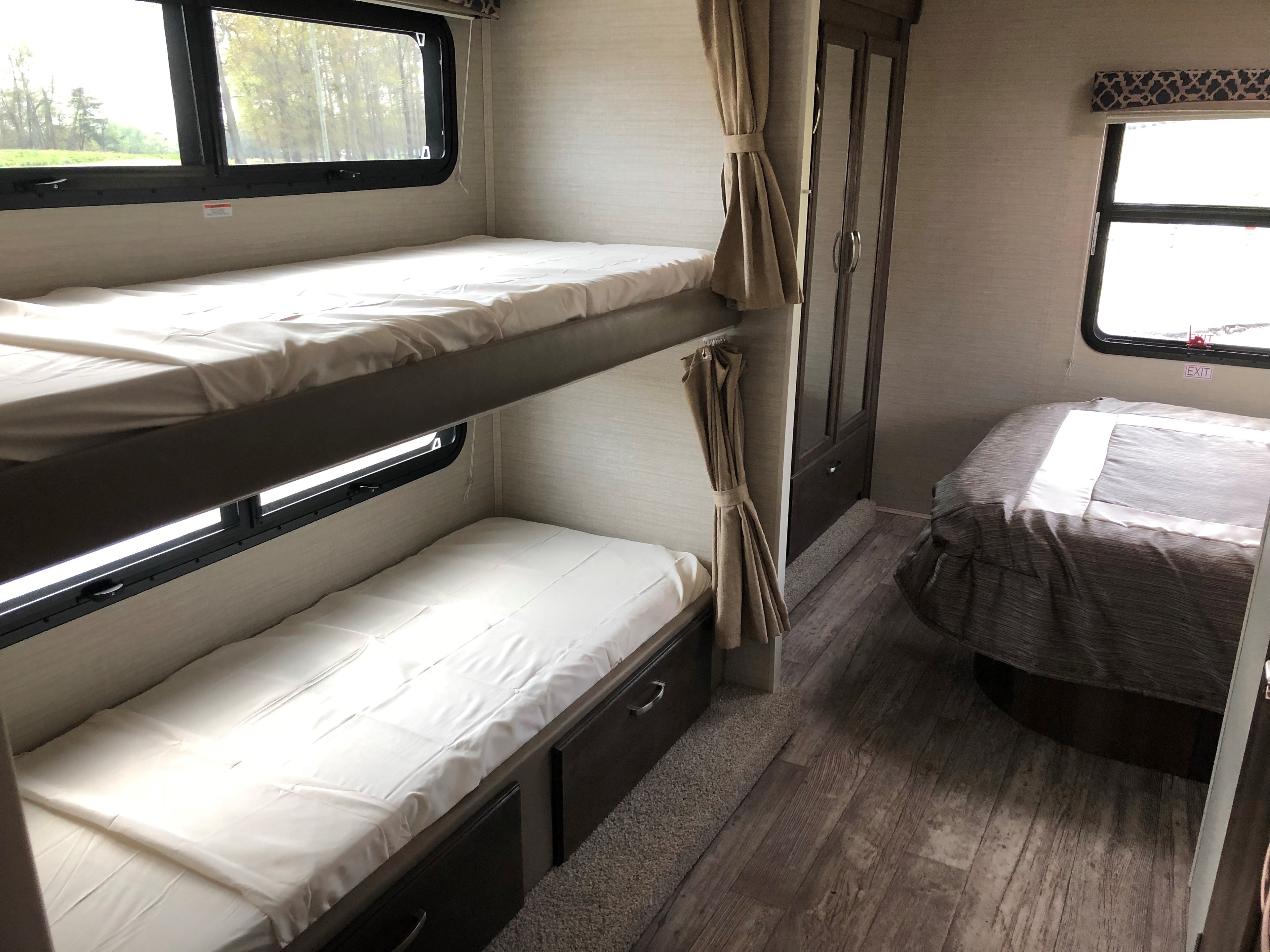 Inside an RV rental: two bunk beds on left, master bed on right. Wood flooring and storage options visible.. Jayco Redhawk 2018