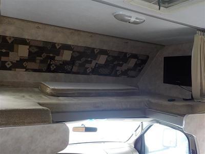 Interior view of an RV rental: a cozy cab-over bunk with mattress and wall-mounted TV.. Gulf Stream Yellowstone 2009