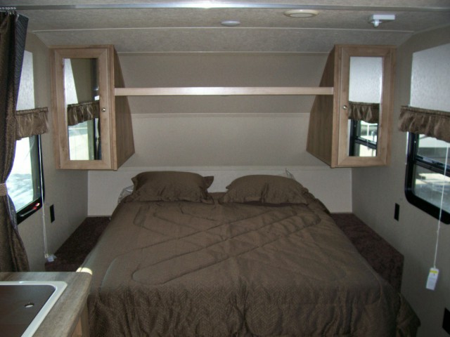 Compact RV rental bedroom with brown bed, overhead cabinets, and windows, ideal for travel trailer adventures.. Palomino Puma 2017
