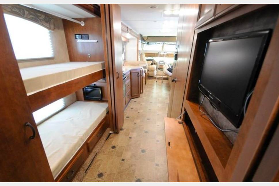 RV rental interior: Bunk beds, central aisle leading to kitchen, and living area with entertainment unit & TV.. Thor Motor Coach Hurricane 2014