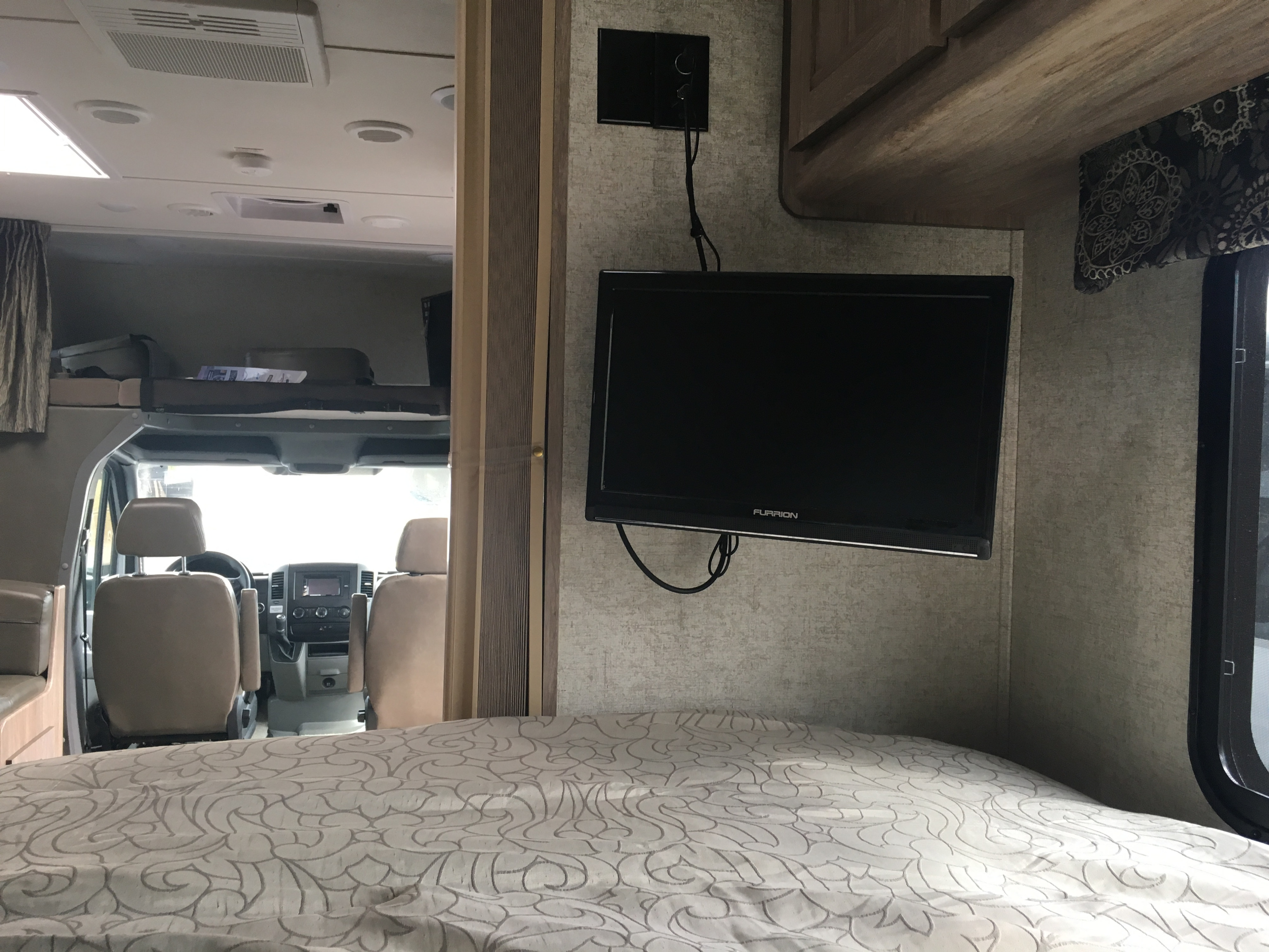Cozy RV rental interior showing a bed, wall-mounted TV, and front driving cab area.. ForestRiver Sunseeker 2018