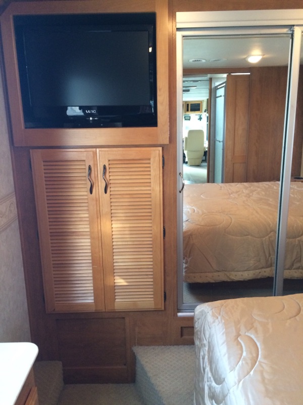RV rental interior: Bedroom with a mounted TV, louvered cabinets, and a mirrored wardrobe reflecting the bed.. Fleetwood Discovery 2005
