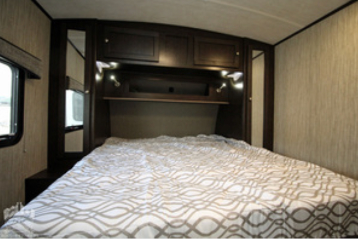 RV rental bedroom: a cozy sleeping area with a bed, overhead cabinets, shelf, and reading lights.. Heartland Sundance 2019