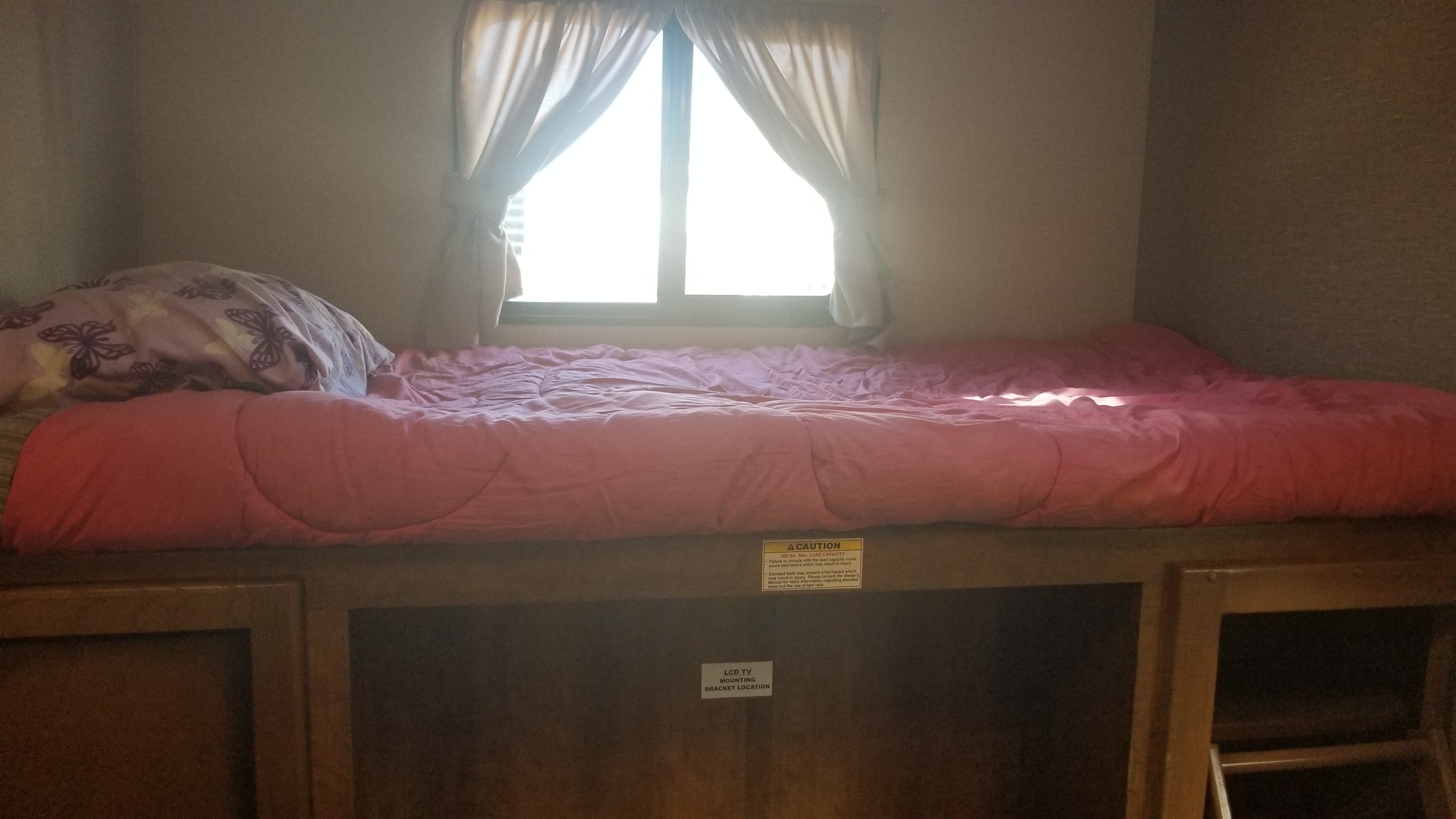 Inside an RV rental bunk: pink bedding, bright window. Note caution for 300lb max & TV mount below.. Crossroads RV Rezerve 2016