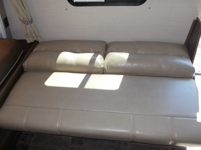 This RV rental features a comfortable, tan, faux-leather sofa that likely converts to a bed, visible with sunlight.. Keystone Bullet 2018