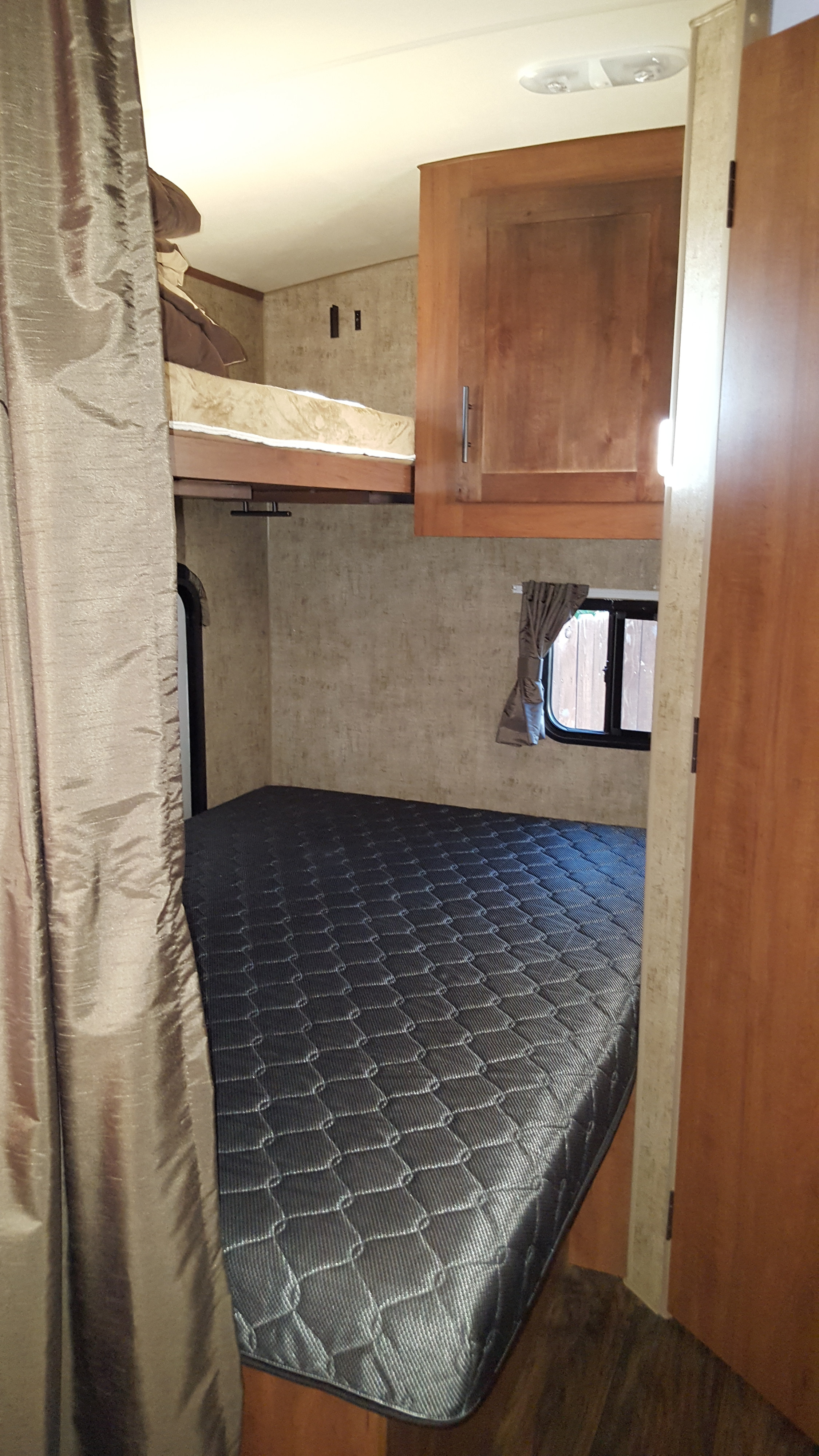 Inside an RV rental bunkhouse: A comfy lower bed, upper bunk, window, and cabinet provide cozy sleeping.. Outdoors Rv Manufacturing Black Rock 2017