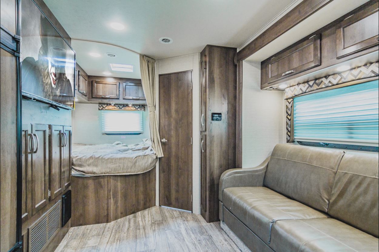 Cozy RV rental interior with bed, sofa, TV, and wood-look flooring. Ample storage is visible throughout.. Jayco Redhawk 2018
